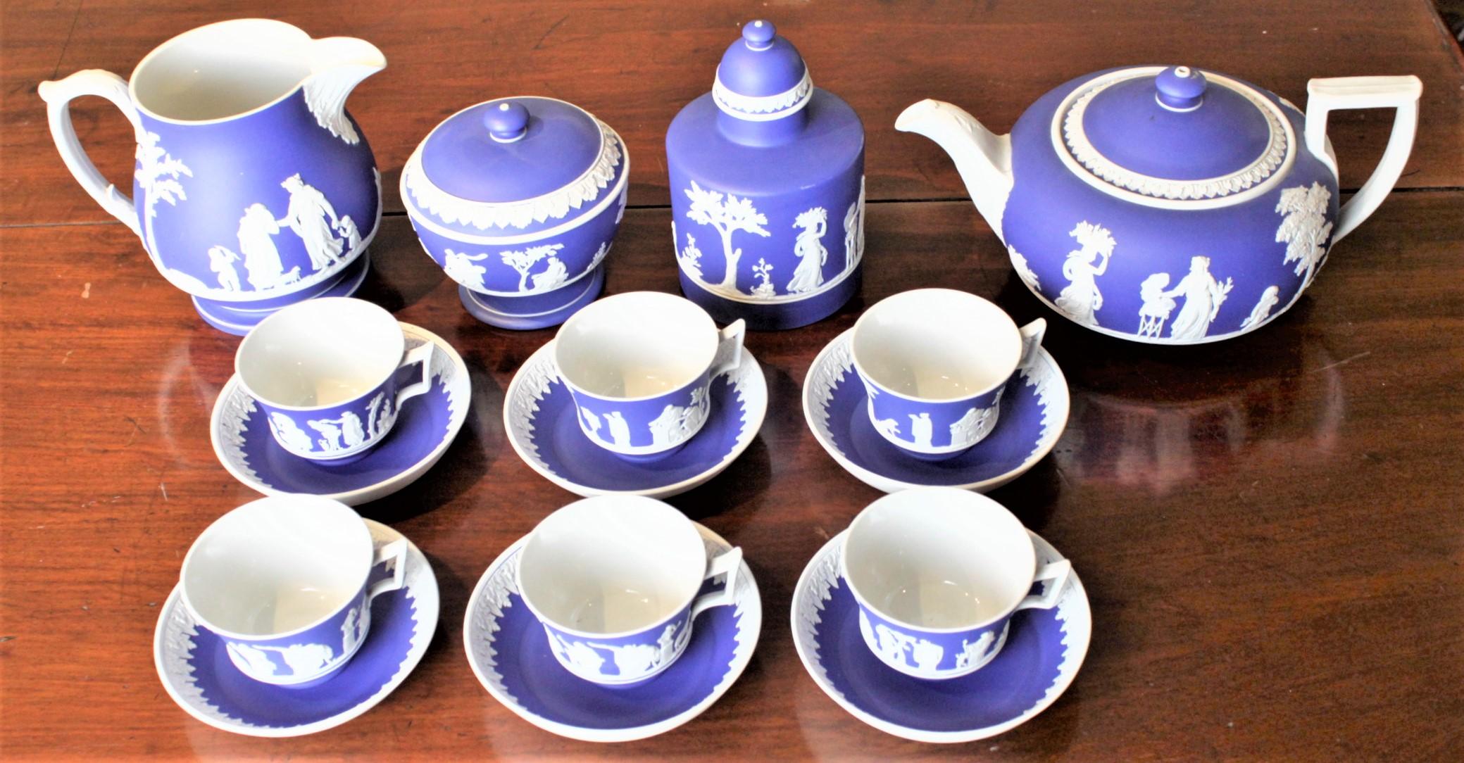 This antique ten piece tea set was made by the renowned Wedgwood Company of England in approximately 1830 in a Neoclassical Revival style. The set is done in an unglazed stoneware 'Jasperware' with white over a deep blue ground. The set is composed