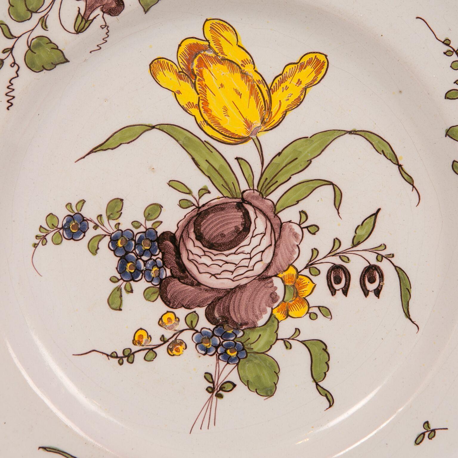 We are pleased to offer this antique Dutch delft charger made in the 18th century, circa 1770. It features a beautiful bouquet of flowers. We see a bright yellow tulip, a peony painted in shades of purple, and other flowers painted in purple, and