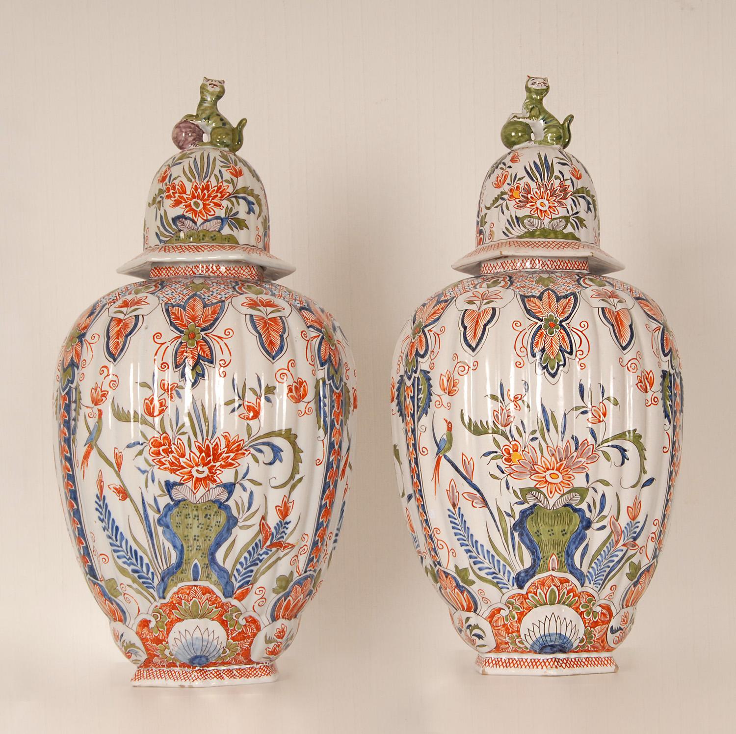 A pair antique Delft vases - Covered Delftware Urns.
Tall decorative covered baluster vases on an octagonal foot.
The ovoid body with four elongated panels painted in blue, iron-red and green with different scenes of exotic bird perched on flowering
