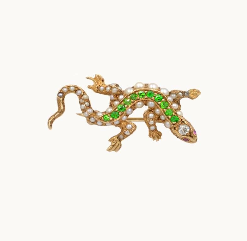 An antique 14 karat yellow gold lizard brooch from circa 1900.  This fantastic brooch is decorated with bright green demantoid garnets along with pearls and features a 0.05 carat diamond in the lizard head. 
This brooch measures approximately 1 inch