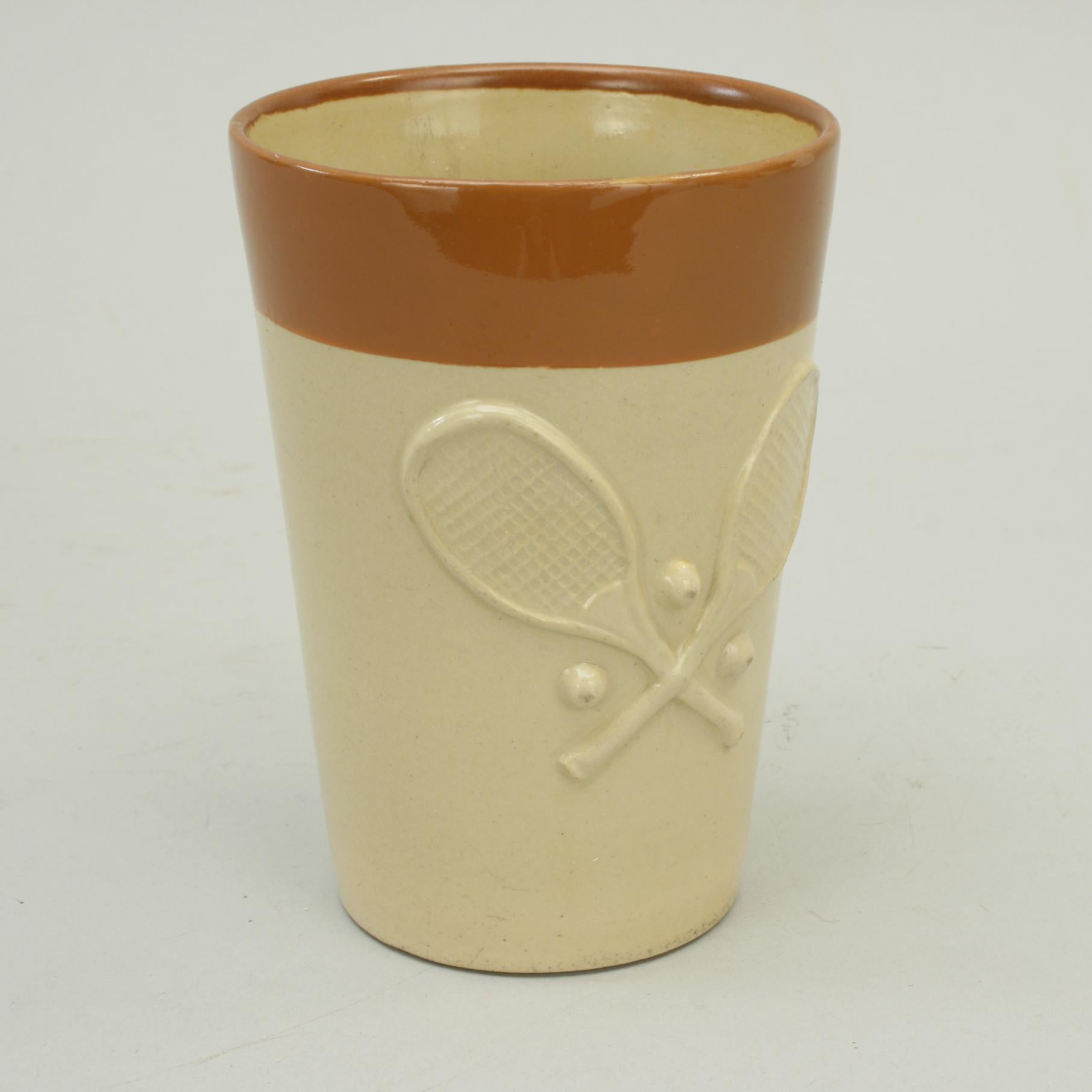 Tennis-themed beaker.
A very nice 'Denby' pottery tennis themed beaker. The tennis ceramic is decorated, in relief, with two crossed convex wedge lawn tennis rackets with three balls. The main body of the cup is pale brown with a treacle brown