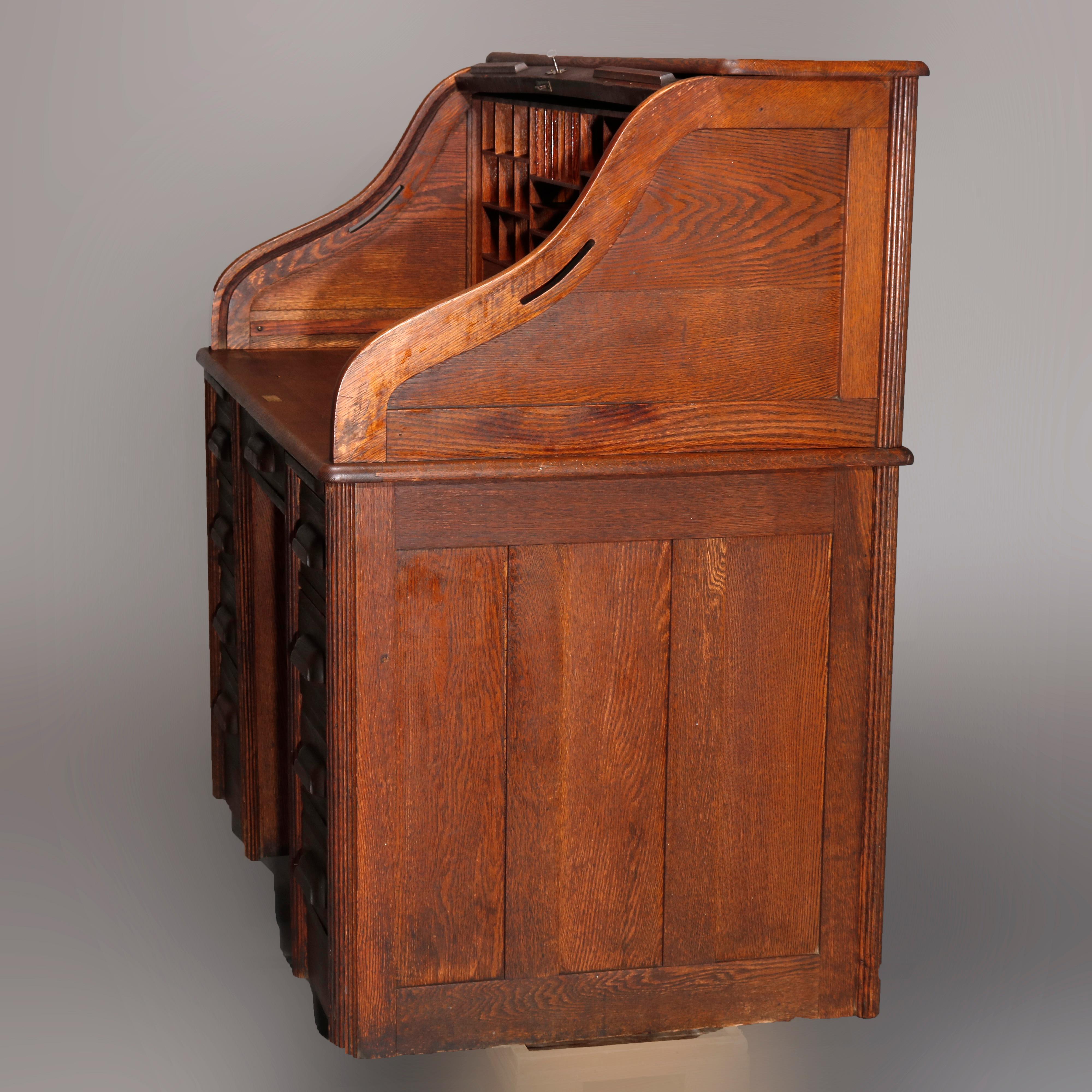 An antique roll top desk in the manner of Derby offers oak construction with serpentine top opening to writing surface with drawers and pigeon holes surmounting paneled case having central frieze drawer and flanking drawer towers with reeded side