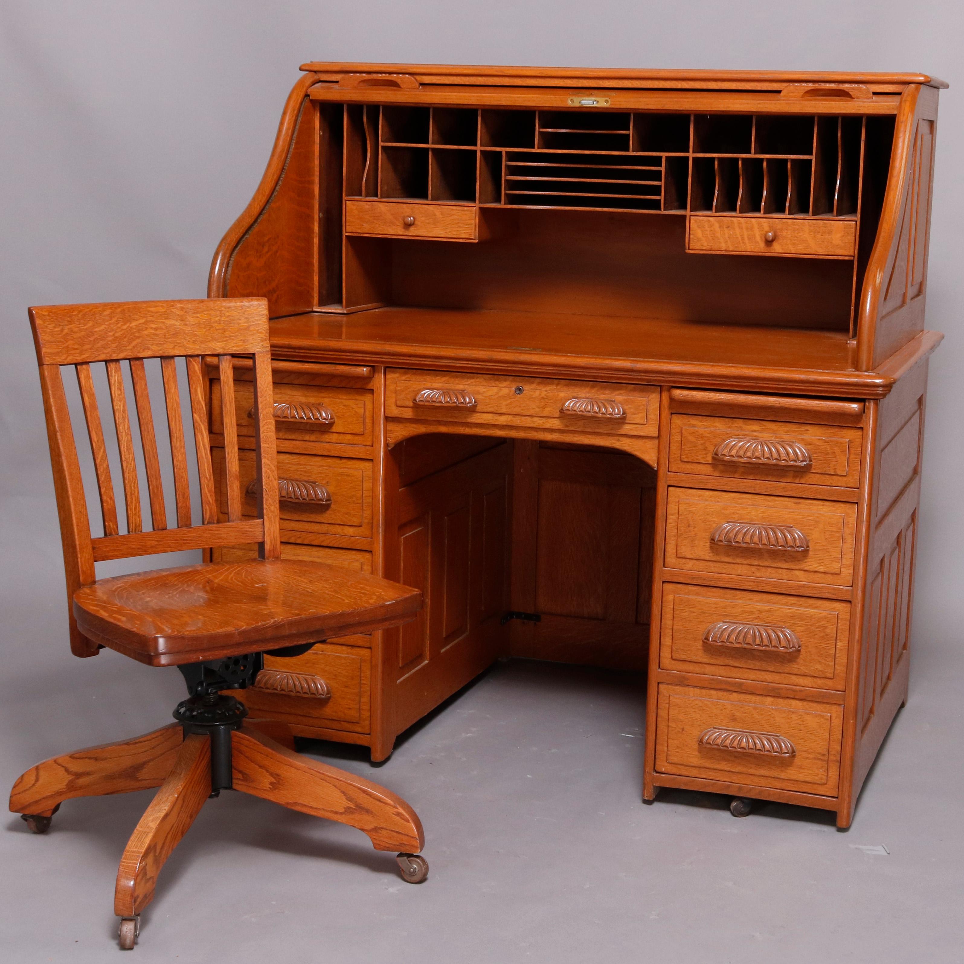 Antique derby school desk by features quarter sawn oak construction with S-form roll top opening to interior pigeon holes and drawers; paneled sides and back; flanking drawer towers; foliate and shell carved cup handles throughout; oak rolling slat
