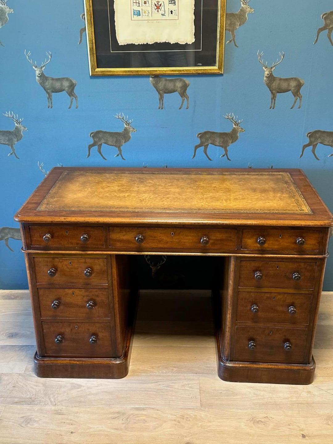 Beautiful small mahogany desk in perfect condition. The desk has 9 drawers and a tan-colored gold-edged leather top. Original wooden knobs on the drawers. Nice warm color. Desk is from the maker Maple & Co (Stamp in drawer), which is known for its