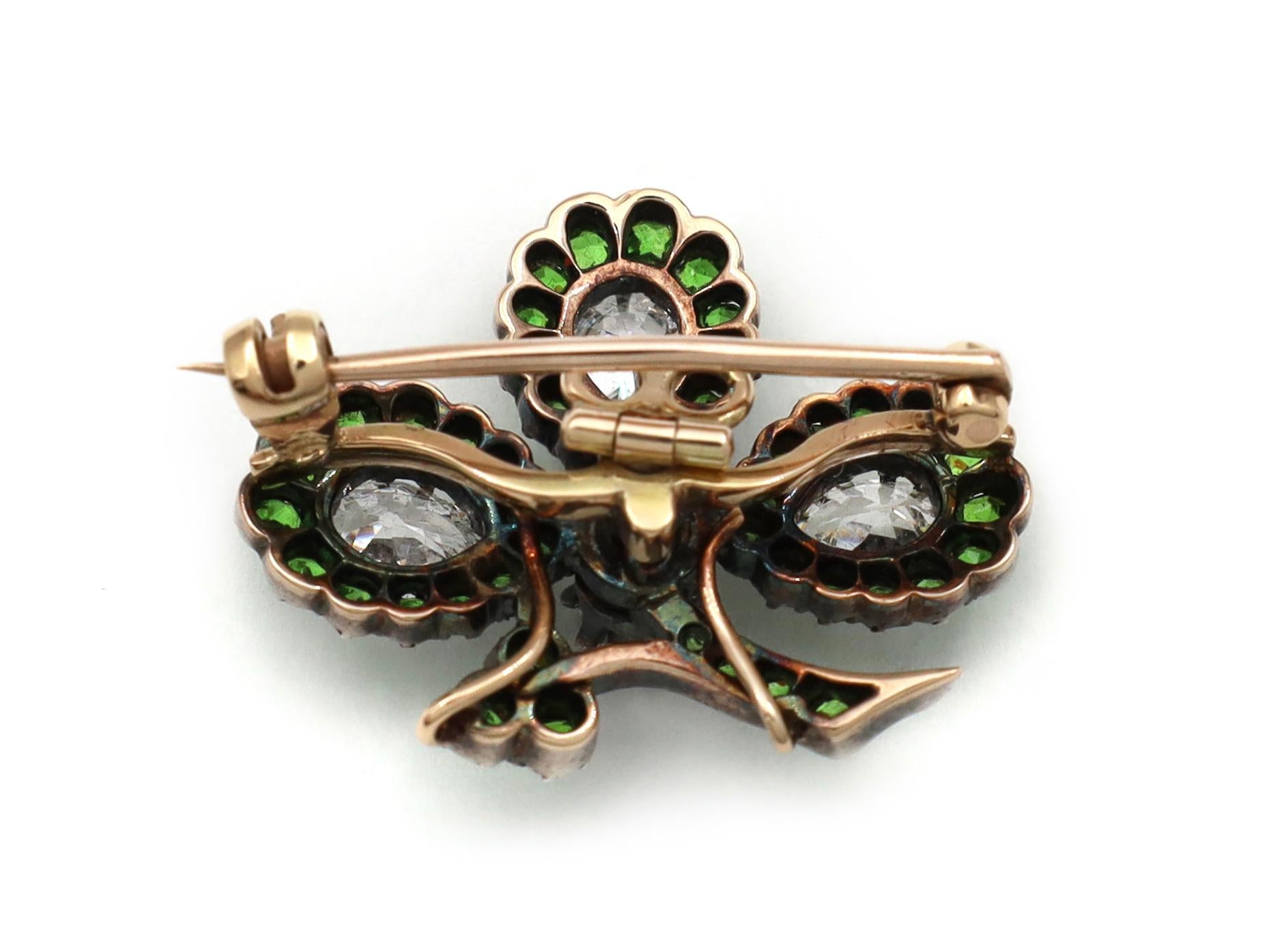 Antique shamrock brooch set with diamonds and demantoid garnets in yellow gold. Set with three estimated 0.52ct pear shape Old cut diamonds in claw settings, centred with an estimated 0.26ct round Old European cut diamond in a raised claw setting,