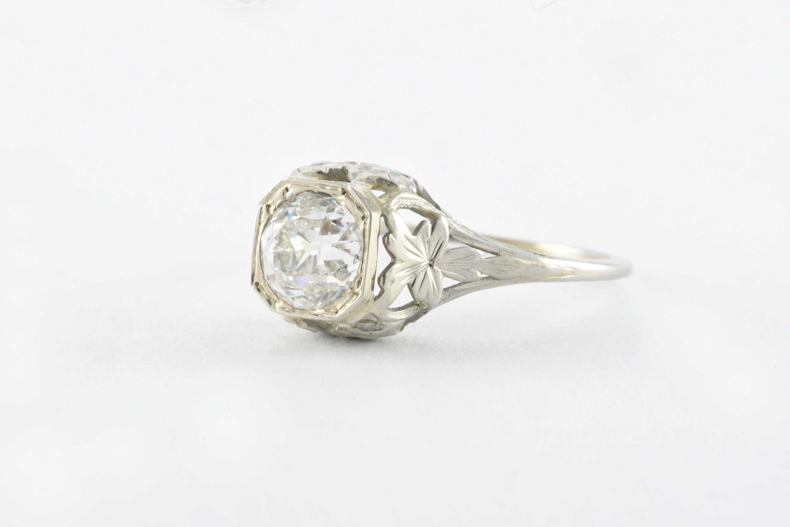 A bold Old European cut diamond measuring approximately 0.98 carats, 5.86 x 5.95 x 4.15mm, H color, VS2-SI1 clarity sits atop a delicate, intricate filigree band fashioned in 18kt white gold. 
