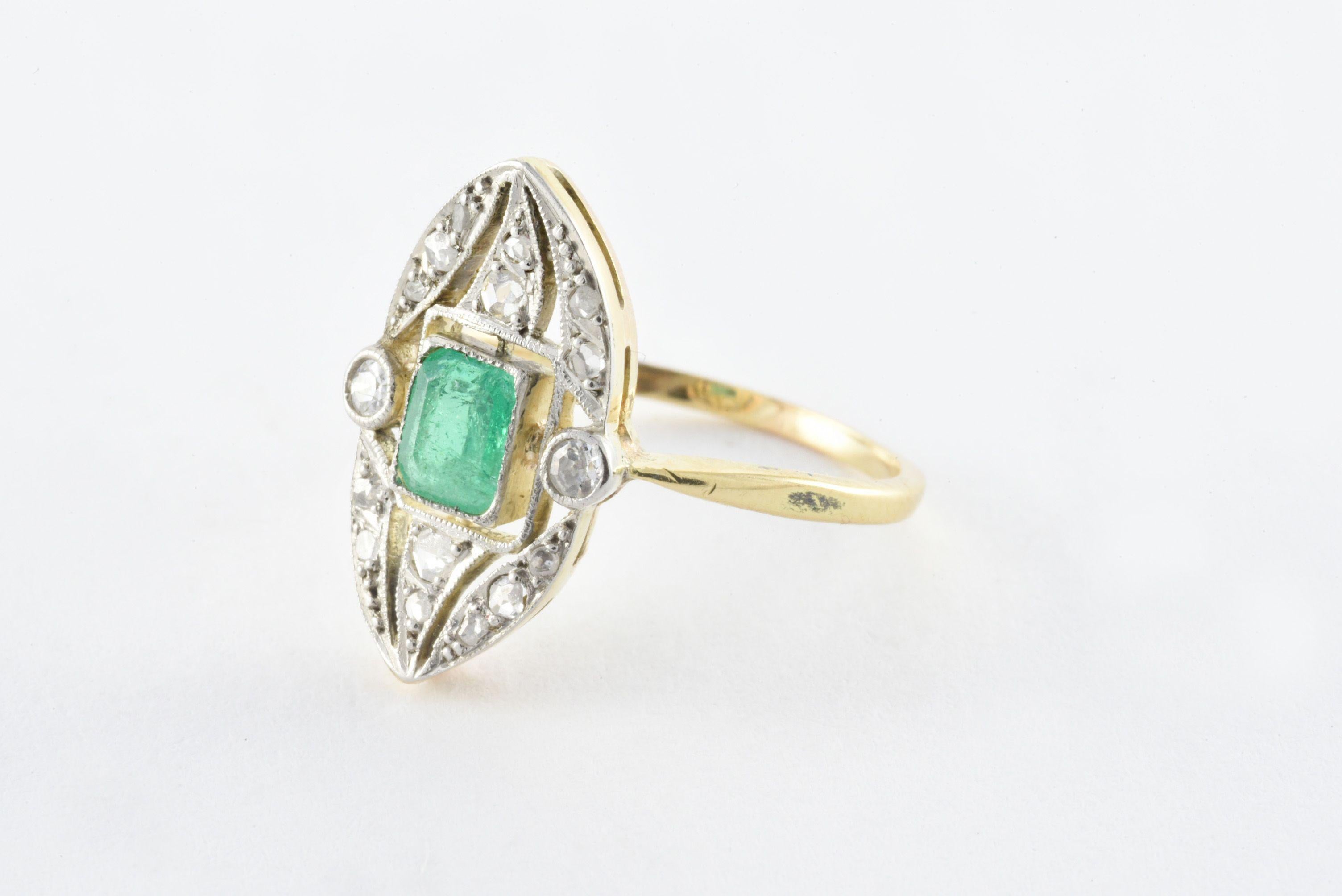 This antique Edwardian-era openwork navette-shaped band highlights a vibrant emerald-shaped green emerald center stone measuring 5 mm X 4 mm, flanked by two single cut diamonds and surrounded by fourteen rose cut diamonds set in 18kt yellow and