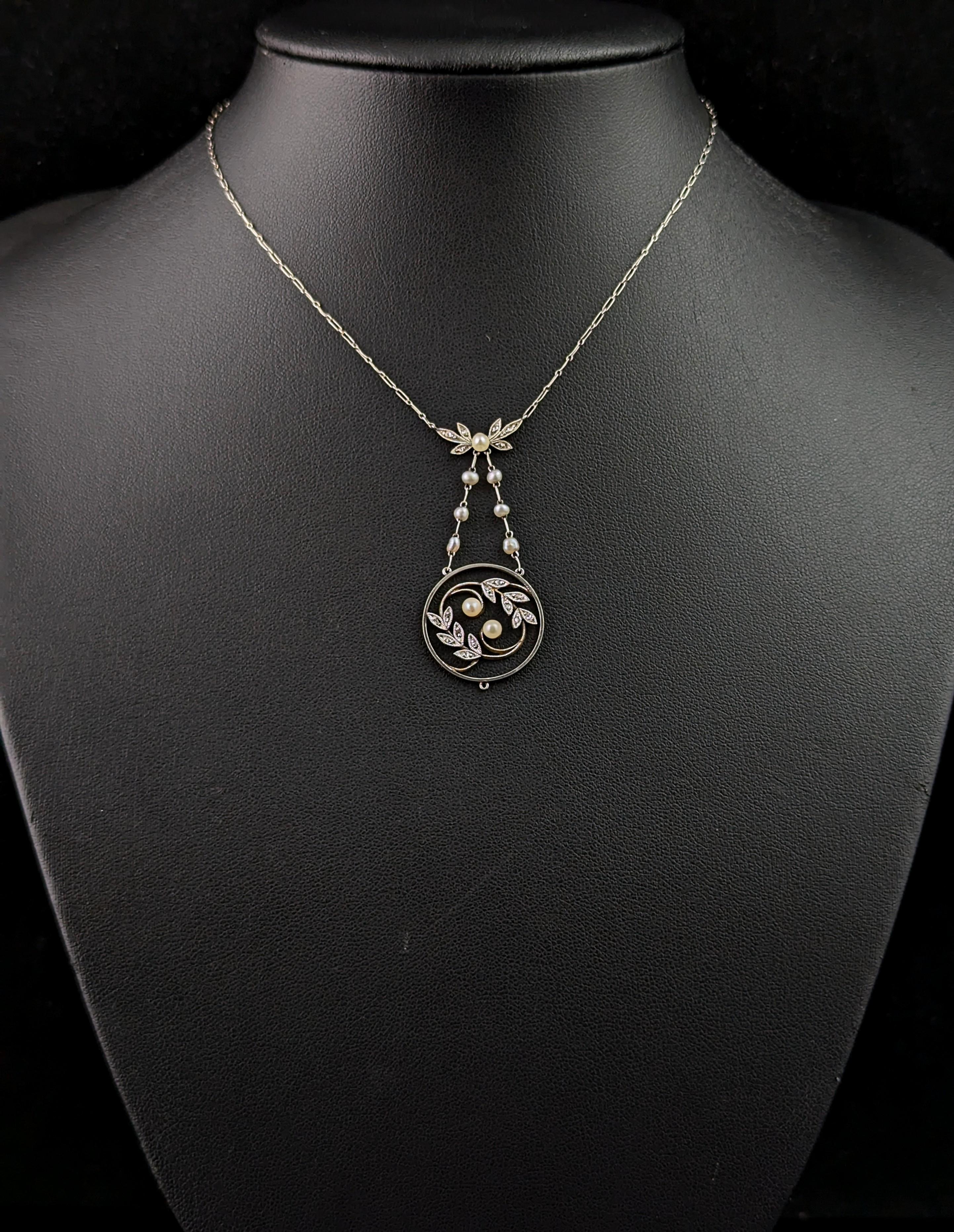 A stunning antique late Edwardian era pendant necklace.

It is a dainty and feminine piece with a circular shaped, open work pendant drop, crafted in cool platinum it is set with sparkling diamond chips and tiny pearls.

It has a paperclip style