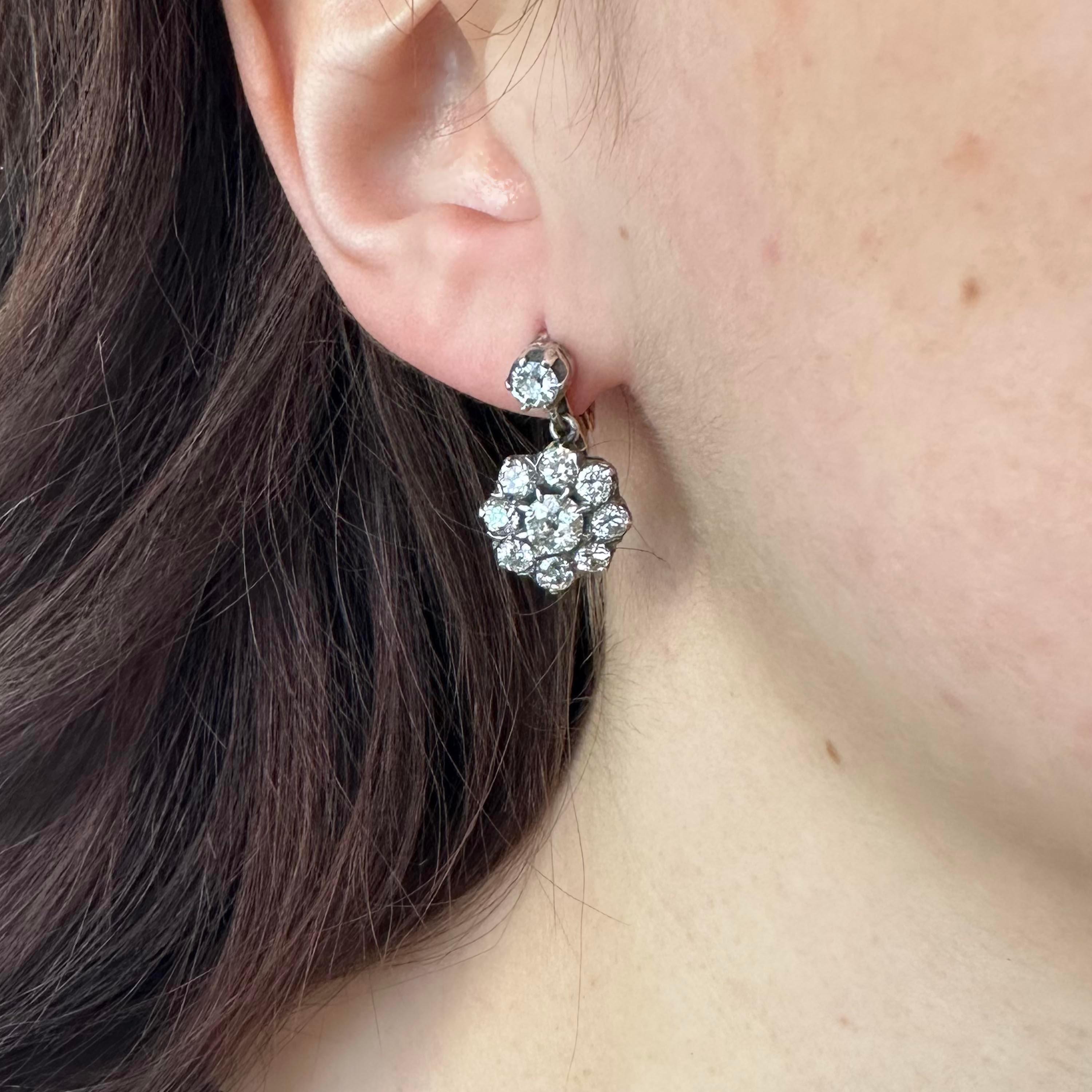 A pair of diamond set silver-upon-gold cluster earrings, with an old-cut diamond in the centre of each pendant drop, surrounded by eight, round brilliant and old-cut diamonds, in silver claw settings, onto a gold gallery, with a single diamond in