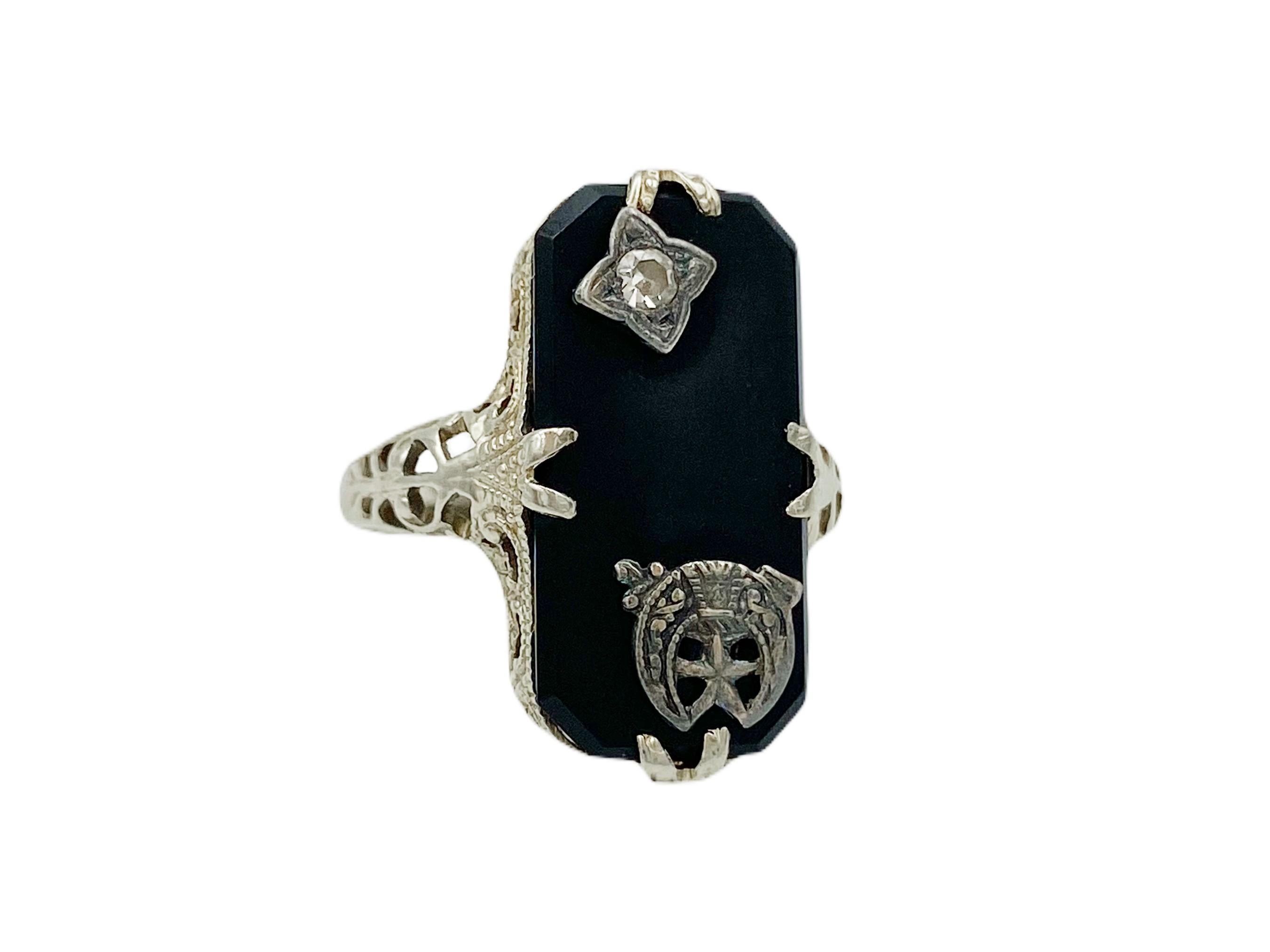 Lovely antique Victorian-era mourning ring in 14k white gold, circa the late 1800s. The face of the ring is a rectangular black onyx with angled corners set with ornate prongs. The onyx is accented with a single-cut 2mm diameter round diamond