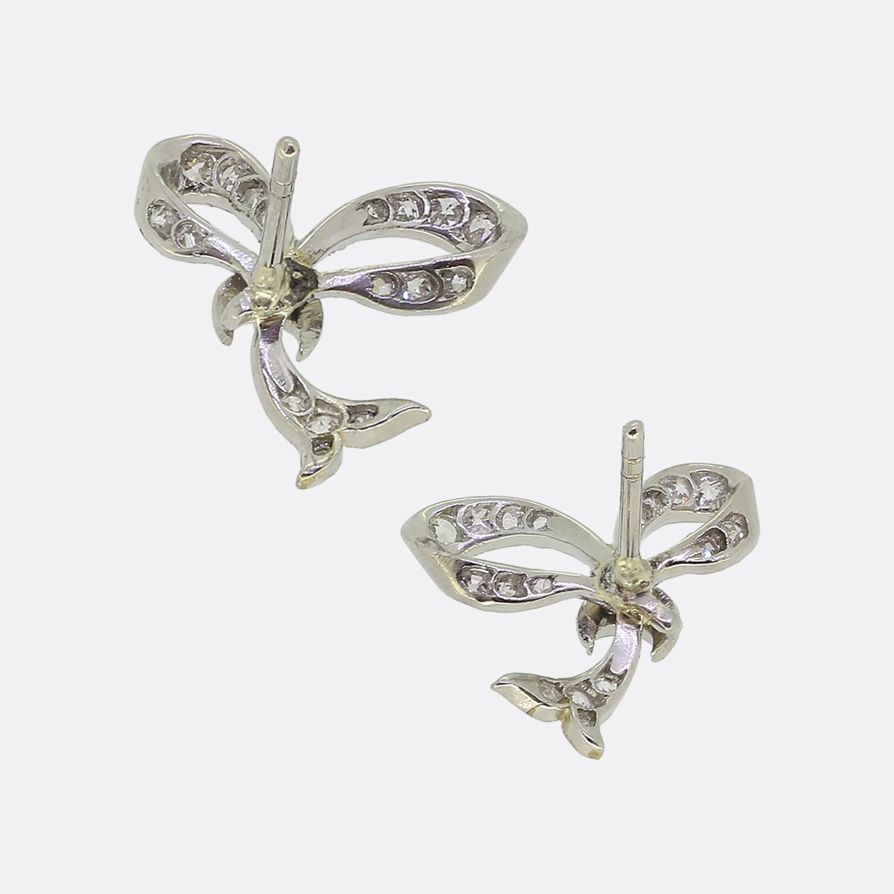 Ecco un elegante paio di orecchini, meticolosamente realizzati in platino. Questi pezzi identici presentano un delicato design a fiocco, incrostato da una serie di piccoli e scintillanti diamanti taglio vecchio e rosa che ne esaltano le curve