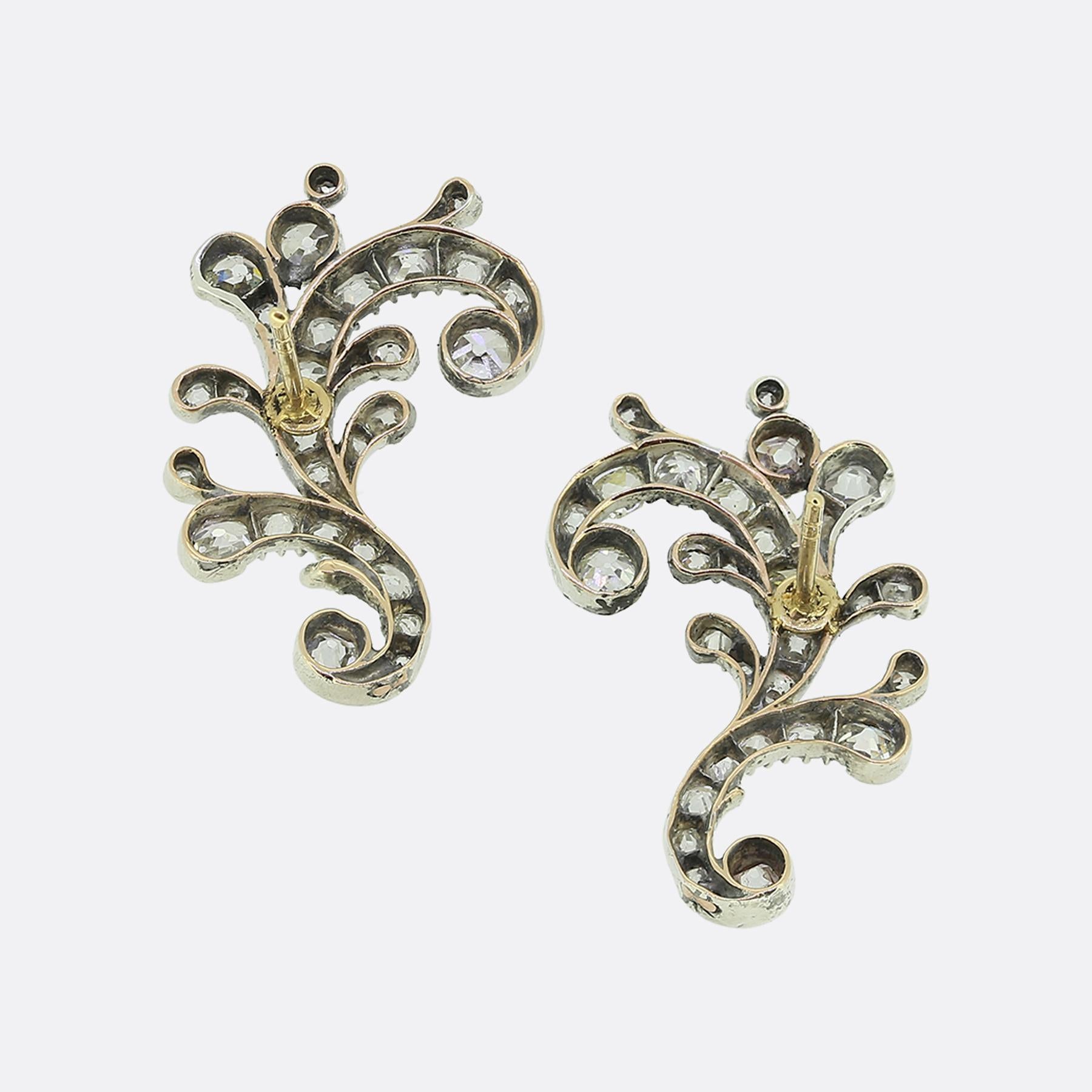 Here we have a distinguished pair of diamond earrings originally dating back to the Victorian period. Meticulously crafted from a blend of 18ct gold and silver, these identical pieces feature a graceful, swirling design adorned with old mine cut