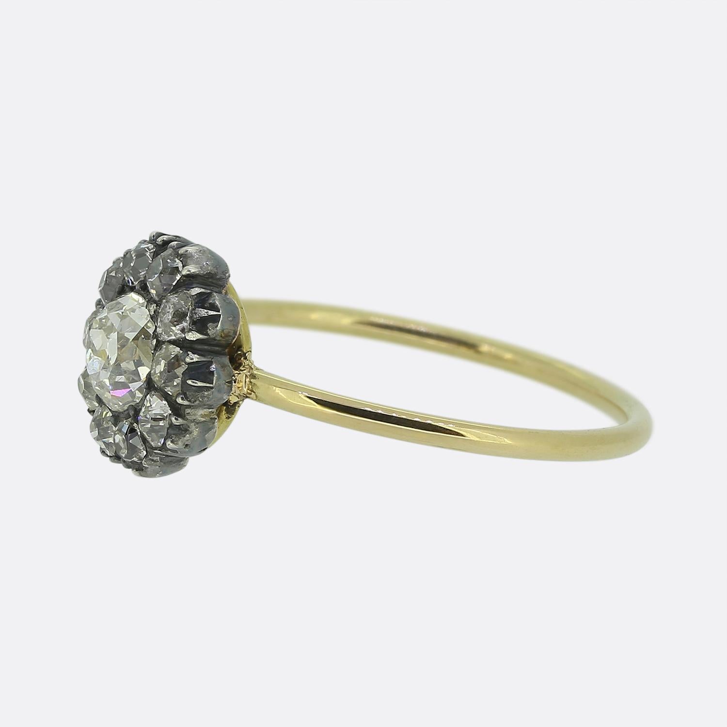 Here we have a charming cluster ring originally dating back to the Victorian period. At the centre of the face we find a single round faceted old mine cut diamond. This chunky principal stone sits slightly risen whilst being surrounded by a frame of