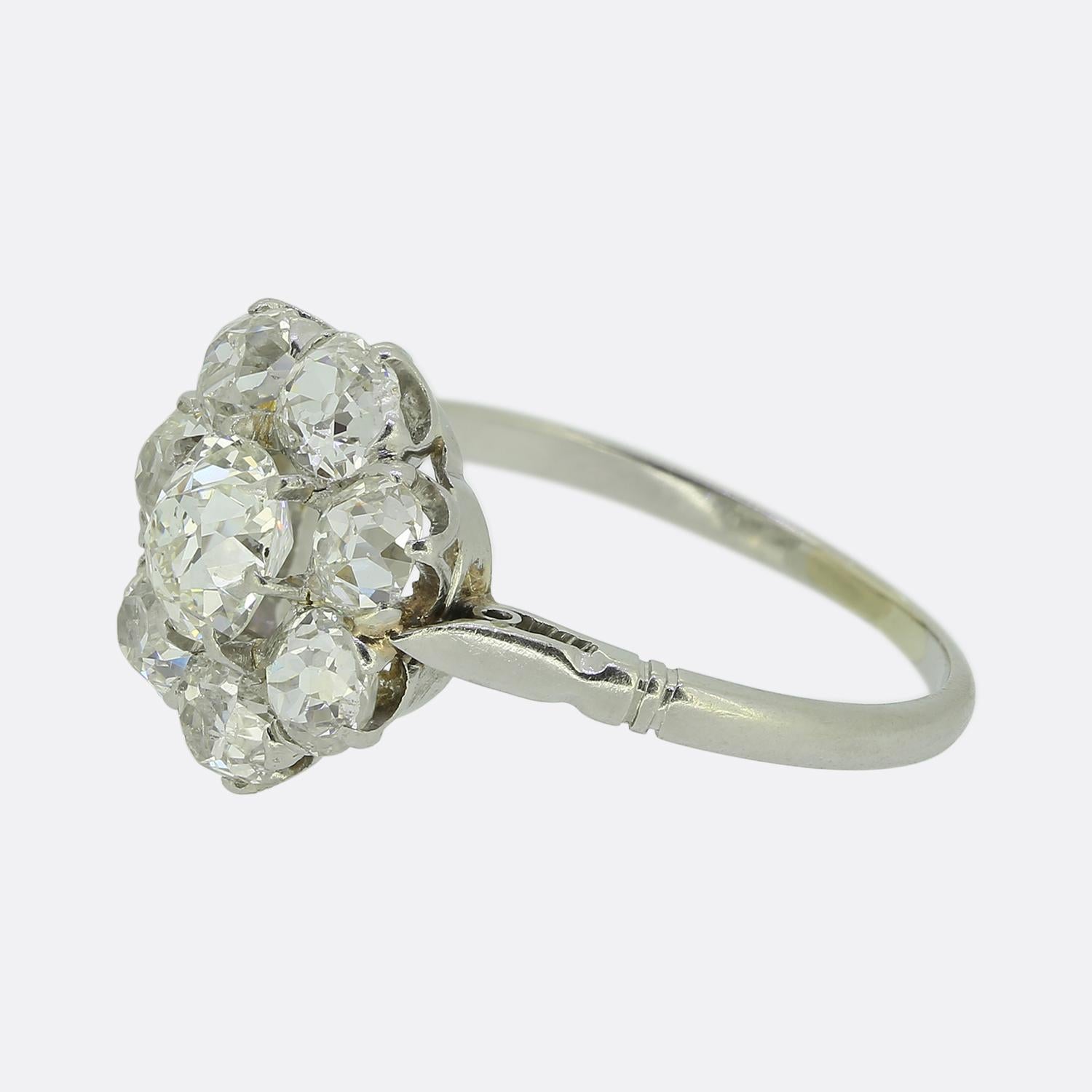 Here we have a stunning antique diamond cluster ring. The design presents a floral arrangement of bright white round faceted old mine cut diamonds; each of which has been meticulously claw set to form a cohesive and elegant look. This classically