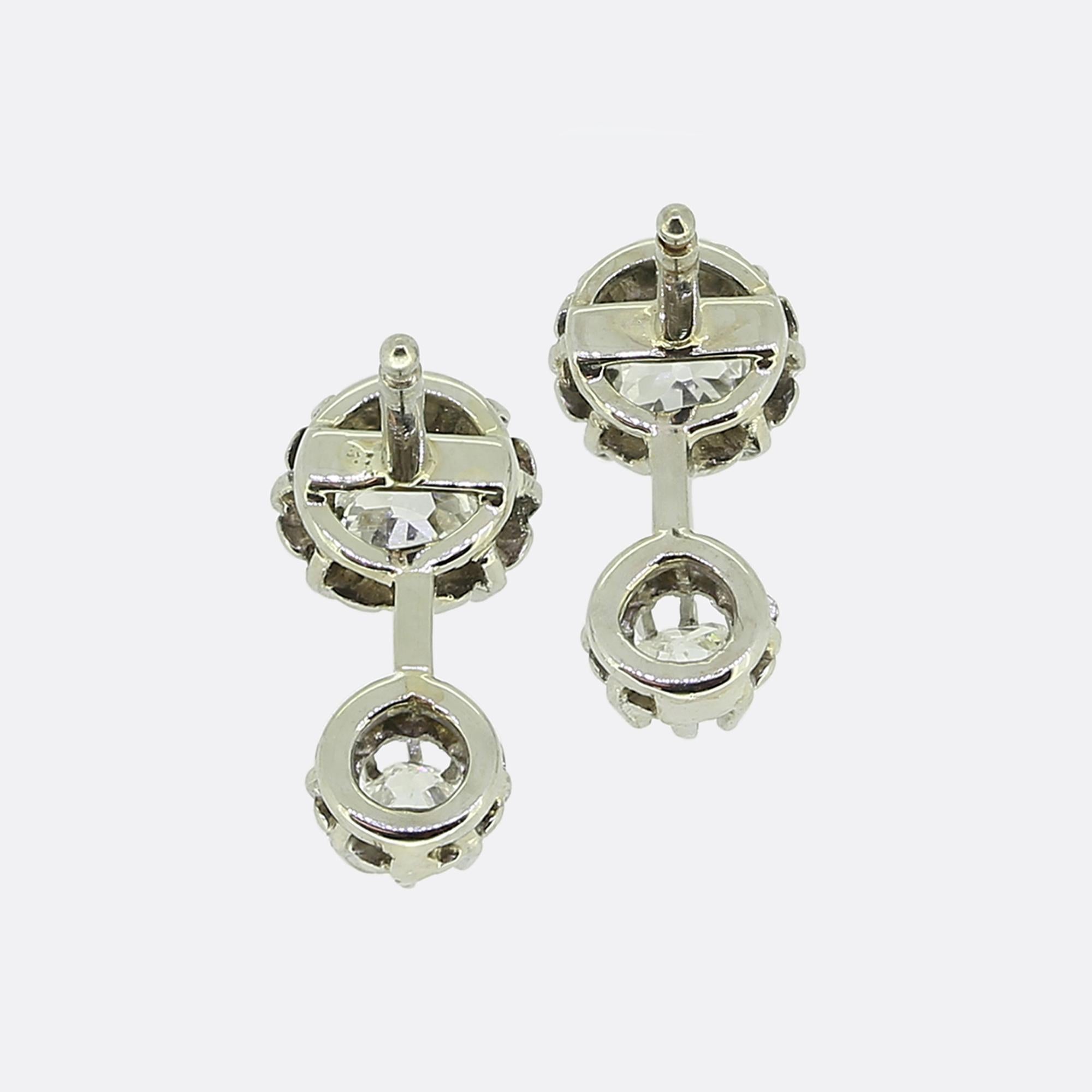 Here we have a charming pair of antique diamond drop earrings. Each identical piece has been crafted from platinum and showcases a duo of round faceted old cut diamonds connected by a slim knife-edged bar at the centre. Each stone has been