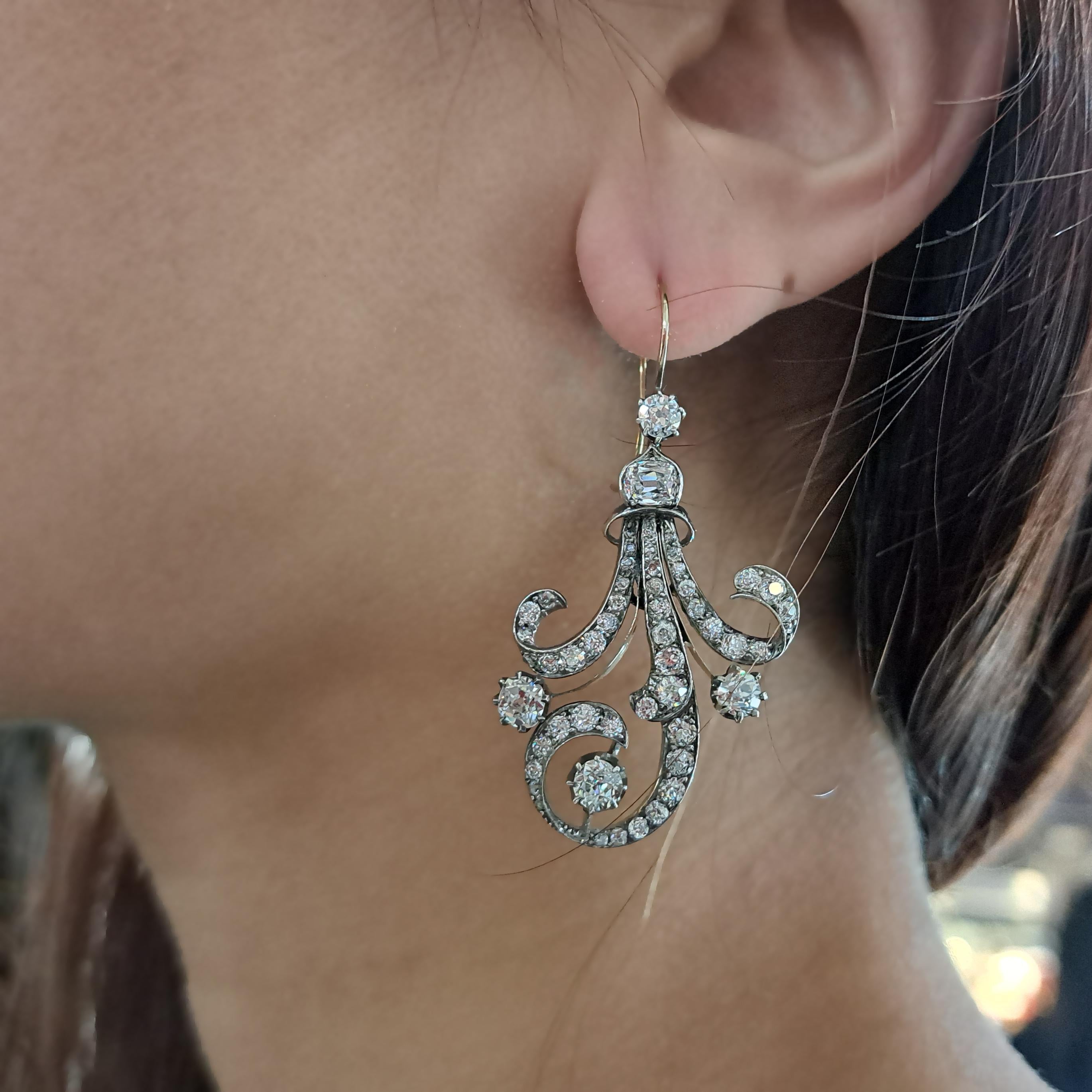 Une paire de boucles d'oreilles anciennes en diamant, montées en argent sur or, serties de diamants de taille ancienne, dans des motifs de balayage et d'enroulement, serties de griffes et de micro-griffes, avec des attaches en forme de crochet. Date