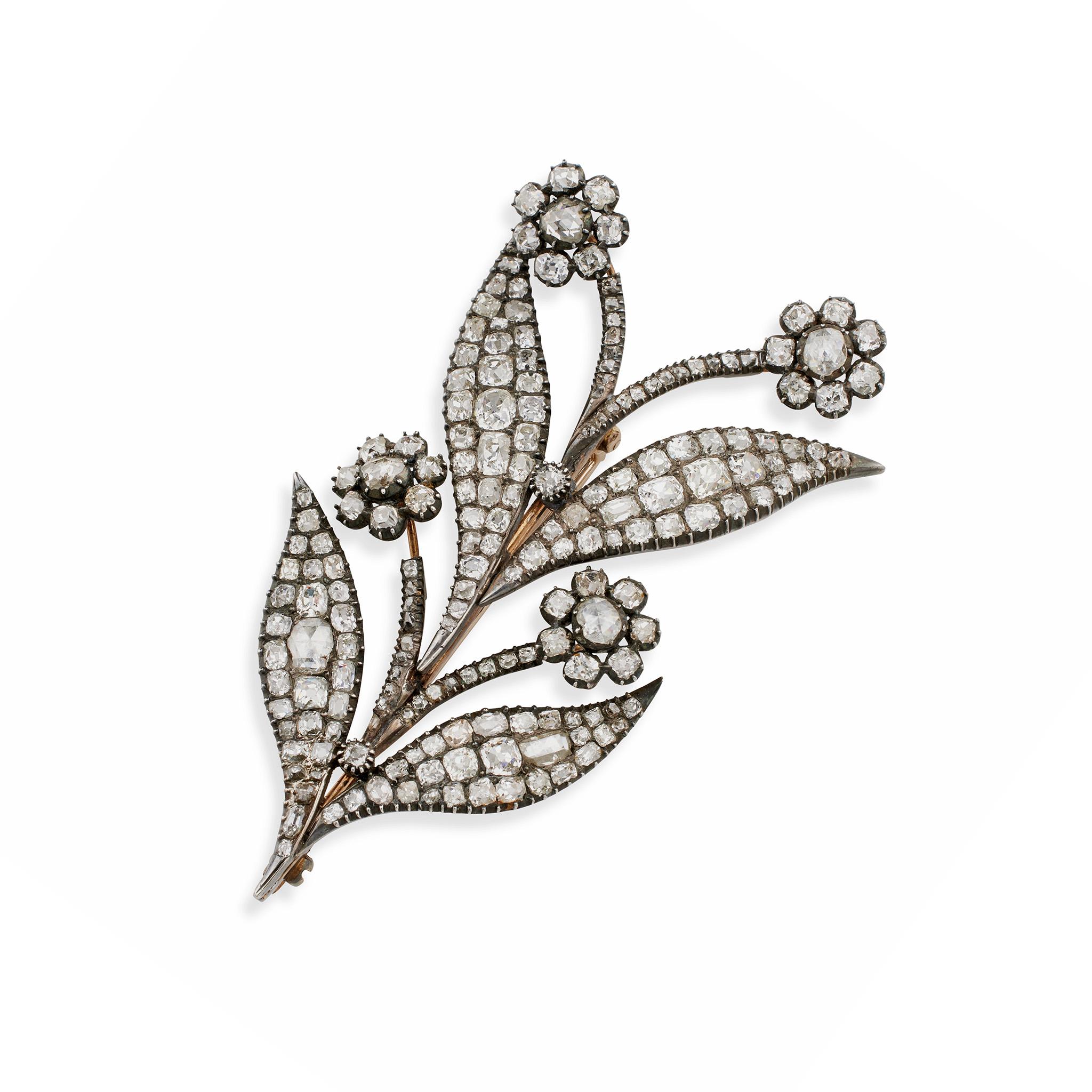 Dating from the mid-19th century, this silver and gold flower brooch is set with over 13 carats of old diamonds. It is designed as a frond of curling leaves and blossoms, set throughout with rectangular and cushion-shaped old mine-cut diamonds, the