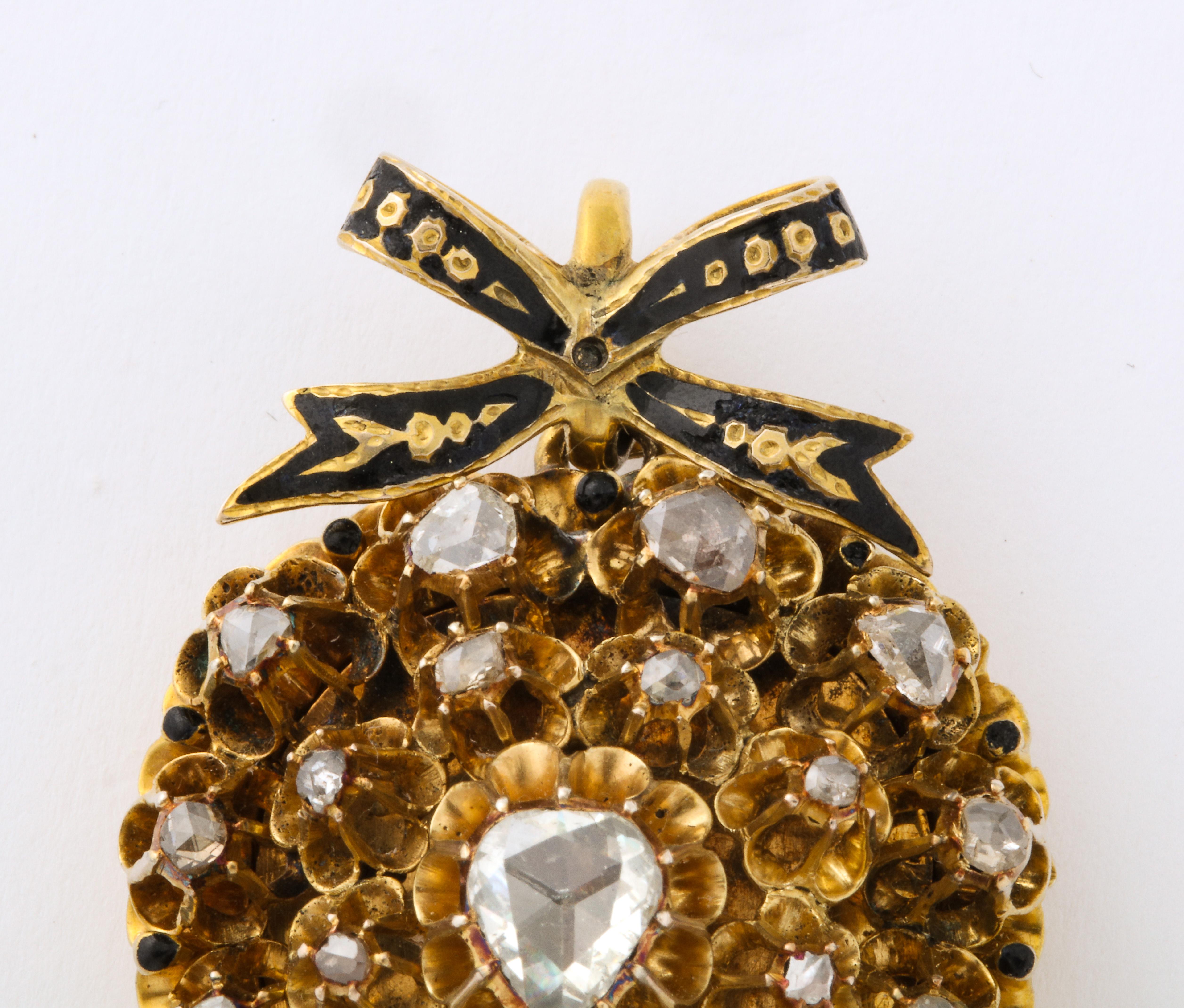 A stunning floral antique rose diamond heart locket with gold petals around a diamond center surround a heart shaped diamond. A French enameled bow sits atop hiding the chain loop. The back reveals a place where a picture was stored behind glass.