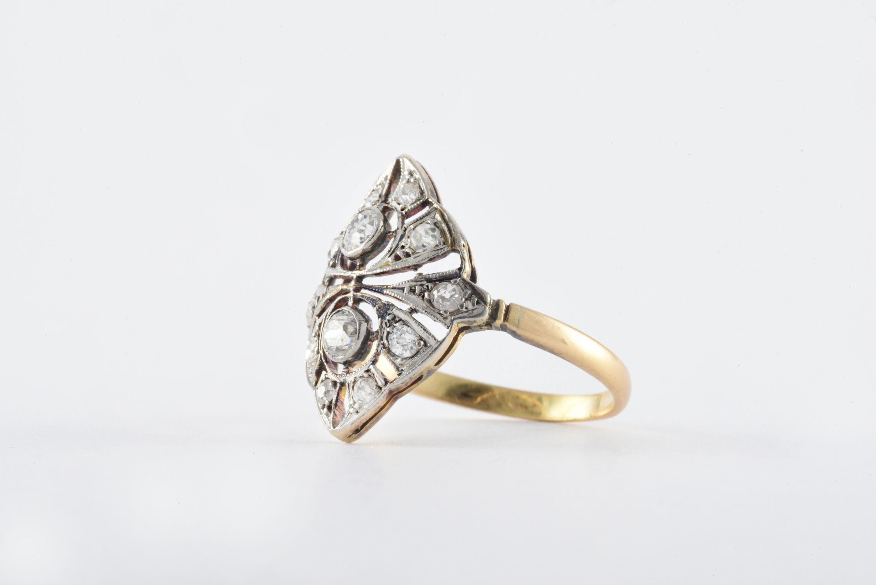 This antique dinner ring features two Old Mine cut diamonds surrounded by a mix of ten Old Mine cut and single cut diamonds set in an elaborate openwork platinum navette-shaped plaque atop an 18kt yellow gold band. The total diamond weight is