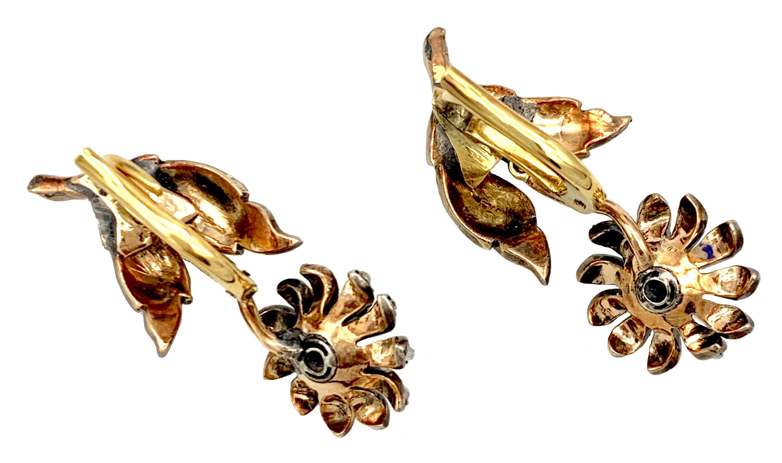 Ces charmantes boucles d'oreilles pendantes sont conçues comme des fleurs en herbe renversées sur une tige avec  feuilles. Les pétales des fleurs et les feuilles sont recouverts de diamants roses sertis en argent sur fond d'or, les tiges des fleurs