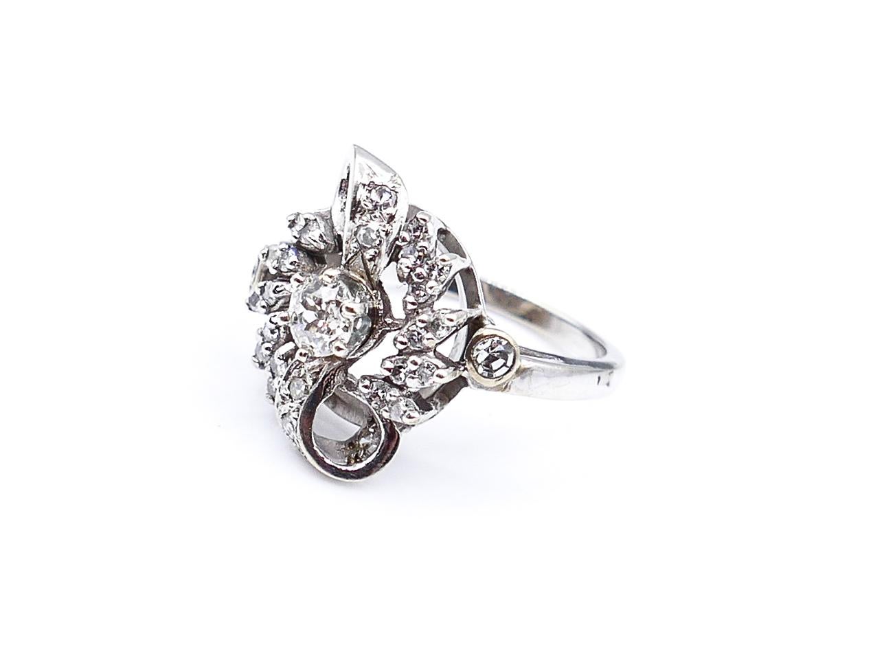 This antique 14 K White Gold ring is made with a prog set center round-cut diamond, weighing 0.75 Carats. The additional 28 Diamonds uniquely coalescing around it, weigh a total of 0.5 carats, and create the feeling that one is looking into an eye