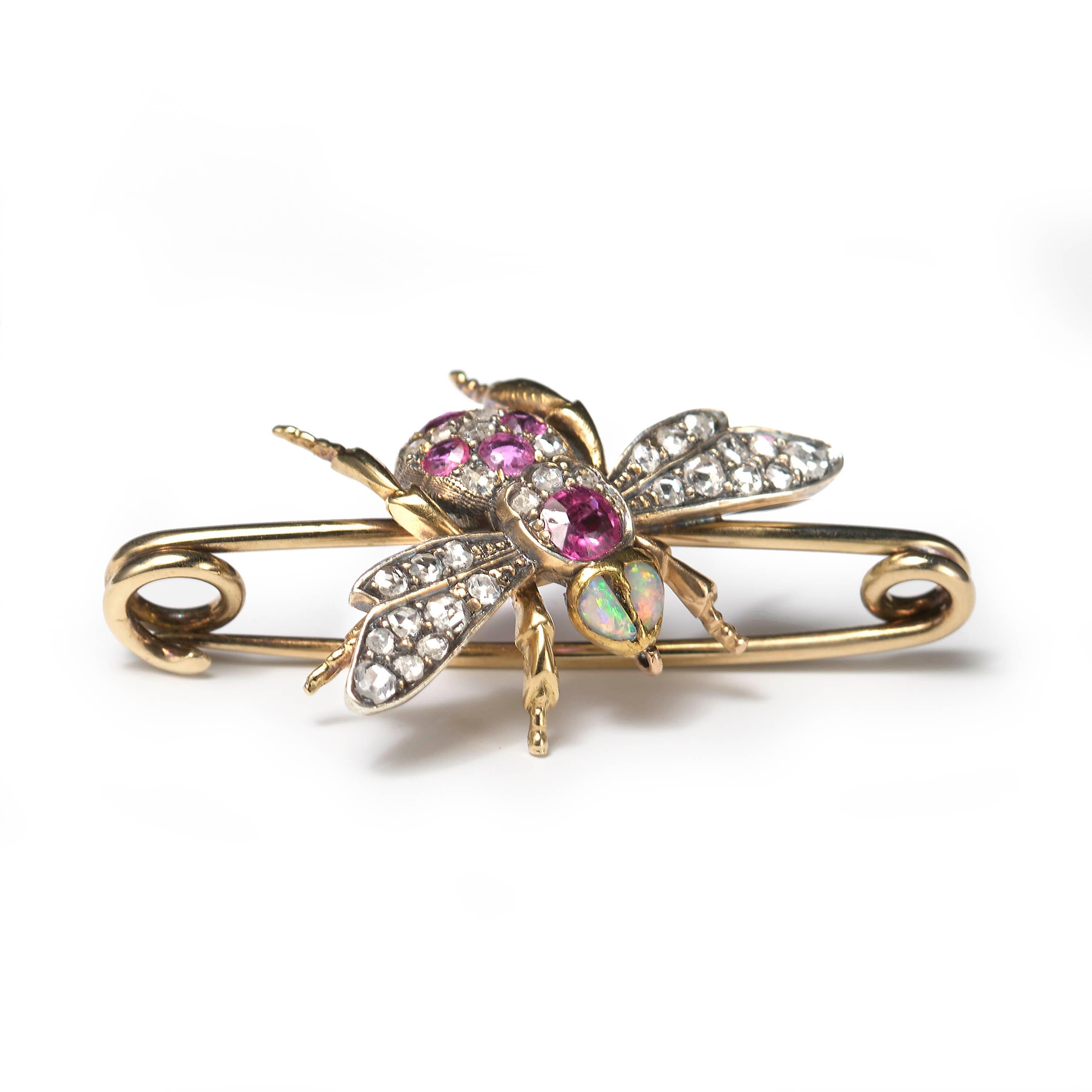 A Victorian bee brooch, set with two opals for the eyes, round and cushion-shaped rubies and rose-cut diamonds to the body, and rose-cut diamonds in the wings, mounted in gold, with silver settings for the wings and set upon a gold bar pin. Circa