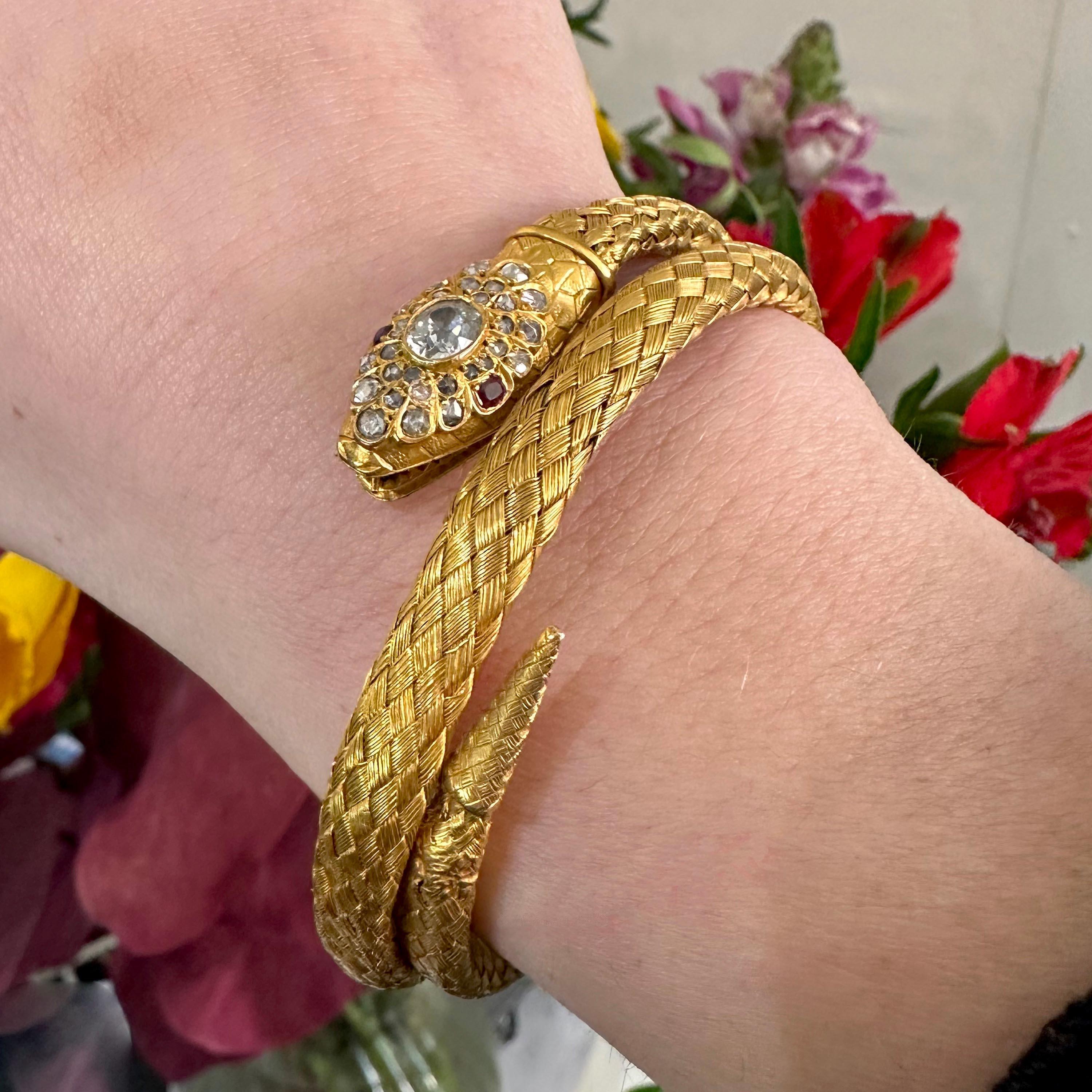 An antique gold coiled snake bracelet, the head is set with an oval, old-cut diamond, in a rub over setting, in a cluster surround of rose-cut diamonds and cushion shaped ruby eyes, it is engraved to represent scales, the open mouth features teeth