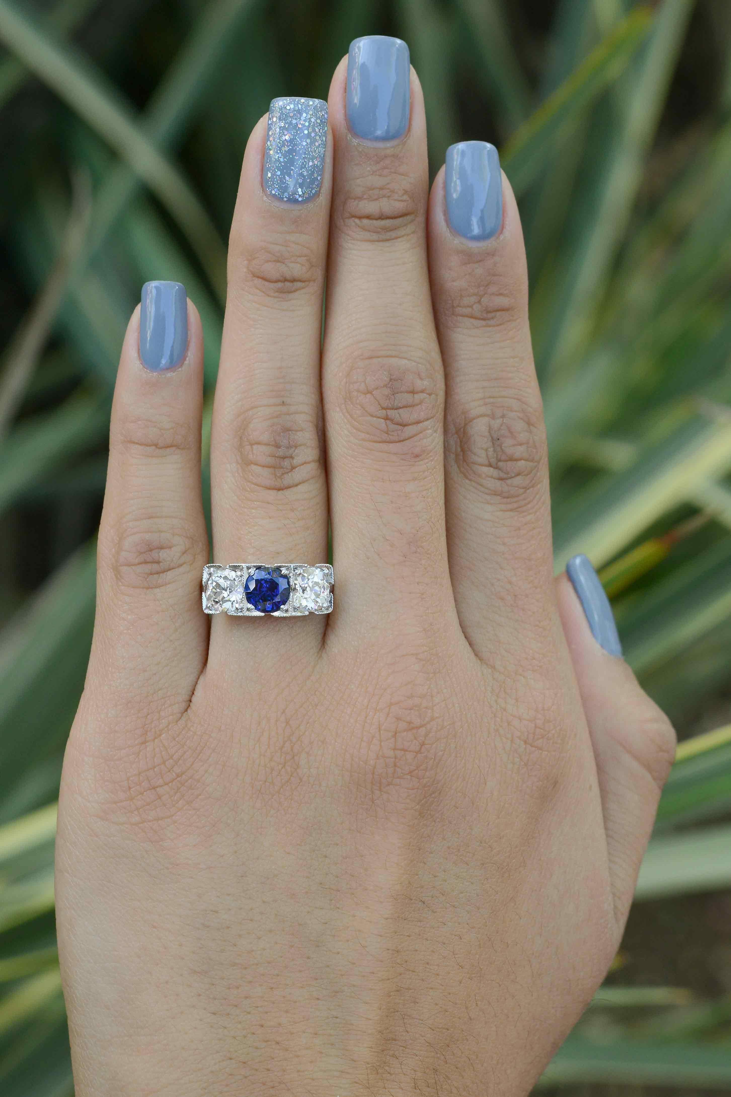 A masterpiece hand engraved antique sapphire and diamond 3 stone engagement ring. The impactful central gemstone is a deeply saturated, lustrous, royal blue sapphire that you can't help being entranced by. Flanked by a significant, matched pair of