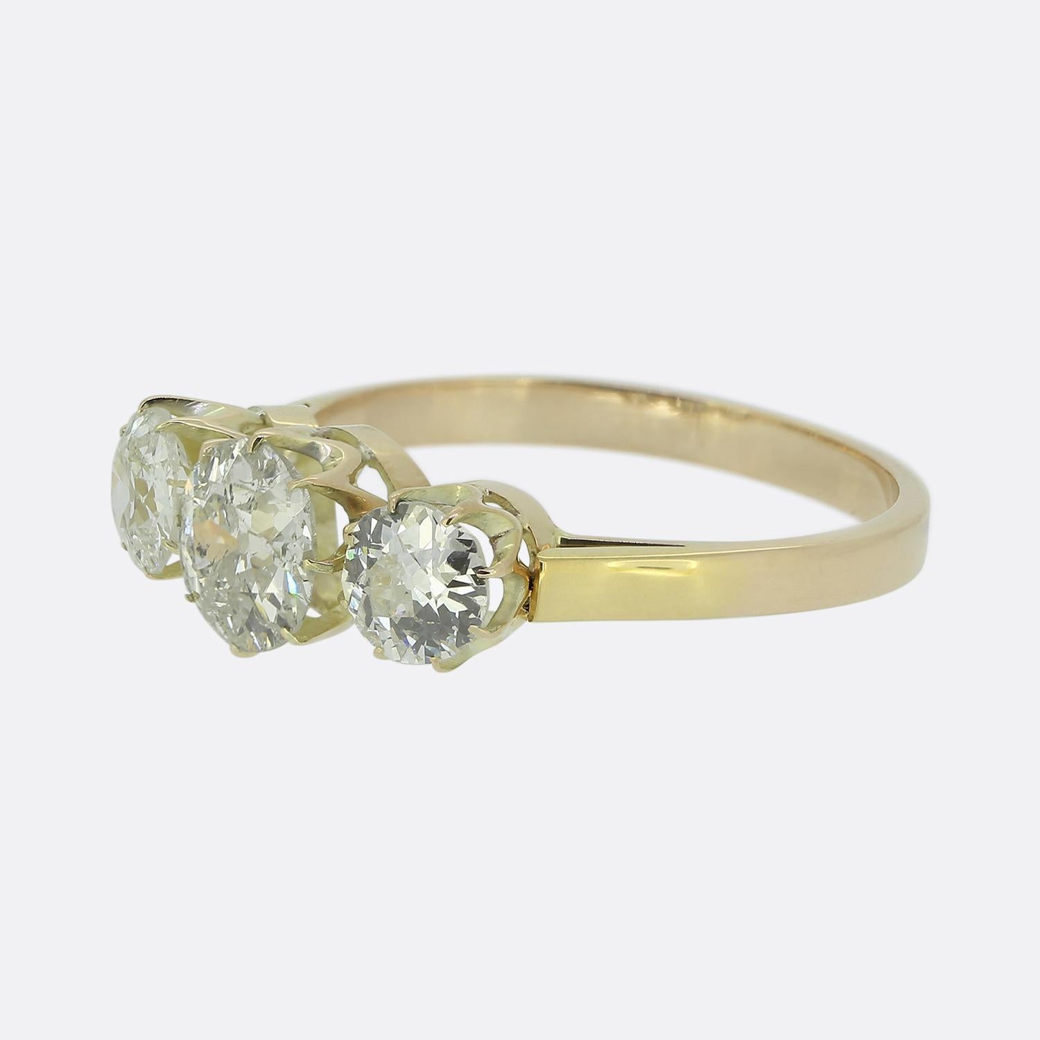 Voici une charmante bague à trois pierres en or jaune 18ct. Le design présente un trio de diamants de taille européenne ancienne, chacun présentant une teinte blanche captivante. Le diamant central est flanqué de deux pierres légèrement plus
