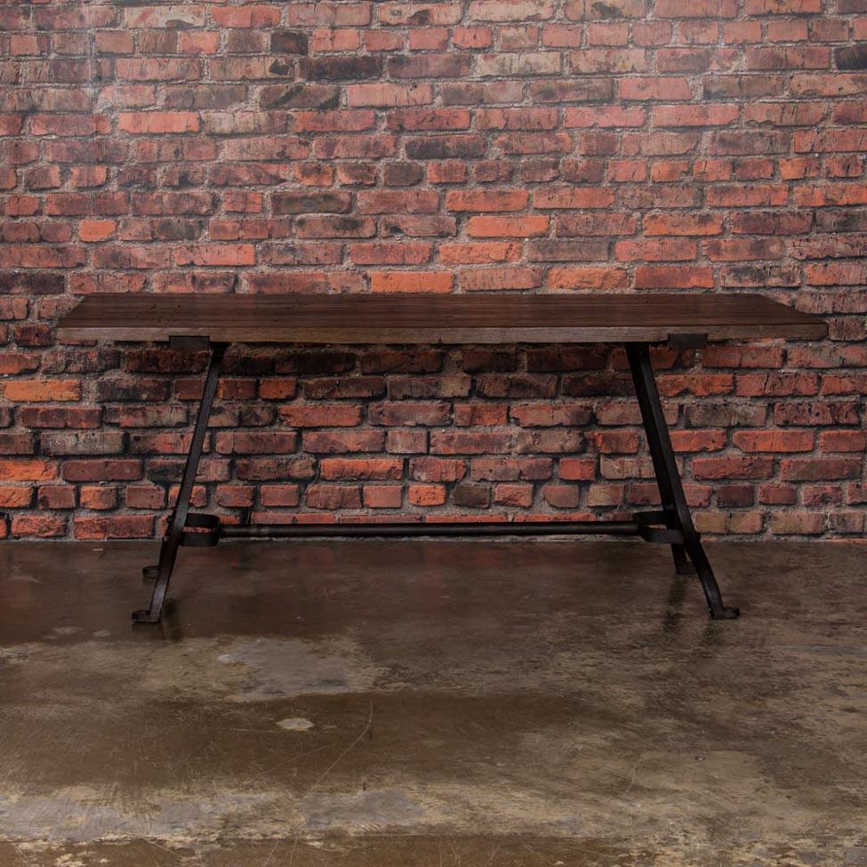 This eastern European dining table with rustic industrial charm, features antique cast iron legs and a hardwood plank top. The distressed top has a rich walnut patina while the base is a dark gray, almost black, waxed iron. The table has been
