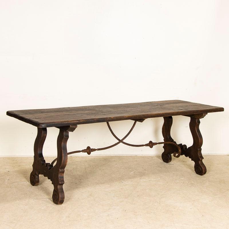 This fascinating table holds visual intrigue due to the carved wood and iron base. Notice the carved harp-shaped sides and curved details accented and supported by the wrought iron scroll work of the unique base. Please examine photos to understand
