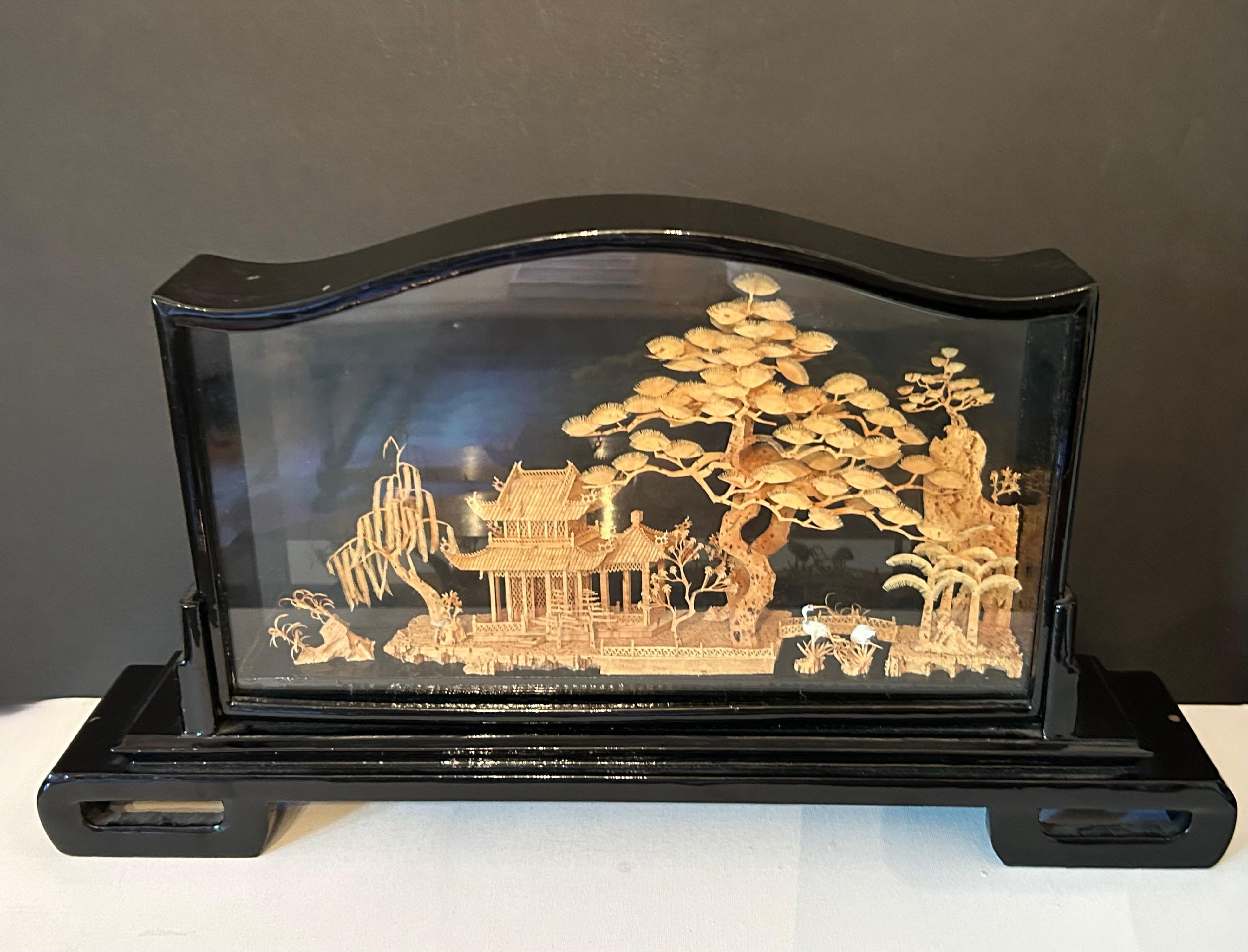 Voici un magnifique bouchon de liège chinois du milieu du siècle dernier.  diorama, présentant un paysage sculpté de manière complexe dans un étagement,  cadre laqué noir. La scène représente une pagode au bord d'une rivière, à l'ombre d'un grand