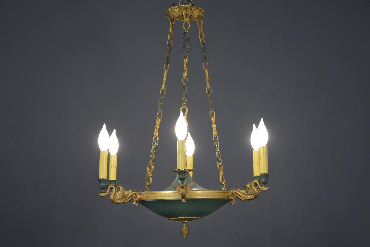 A remarkable antique empire chandelier crafted out of bronze is in good condition and features a gold-plated finish. It comes with a combination of French pale green paint color with a beautiful patina finish, six lights holding by swan motifs, has