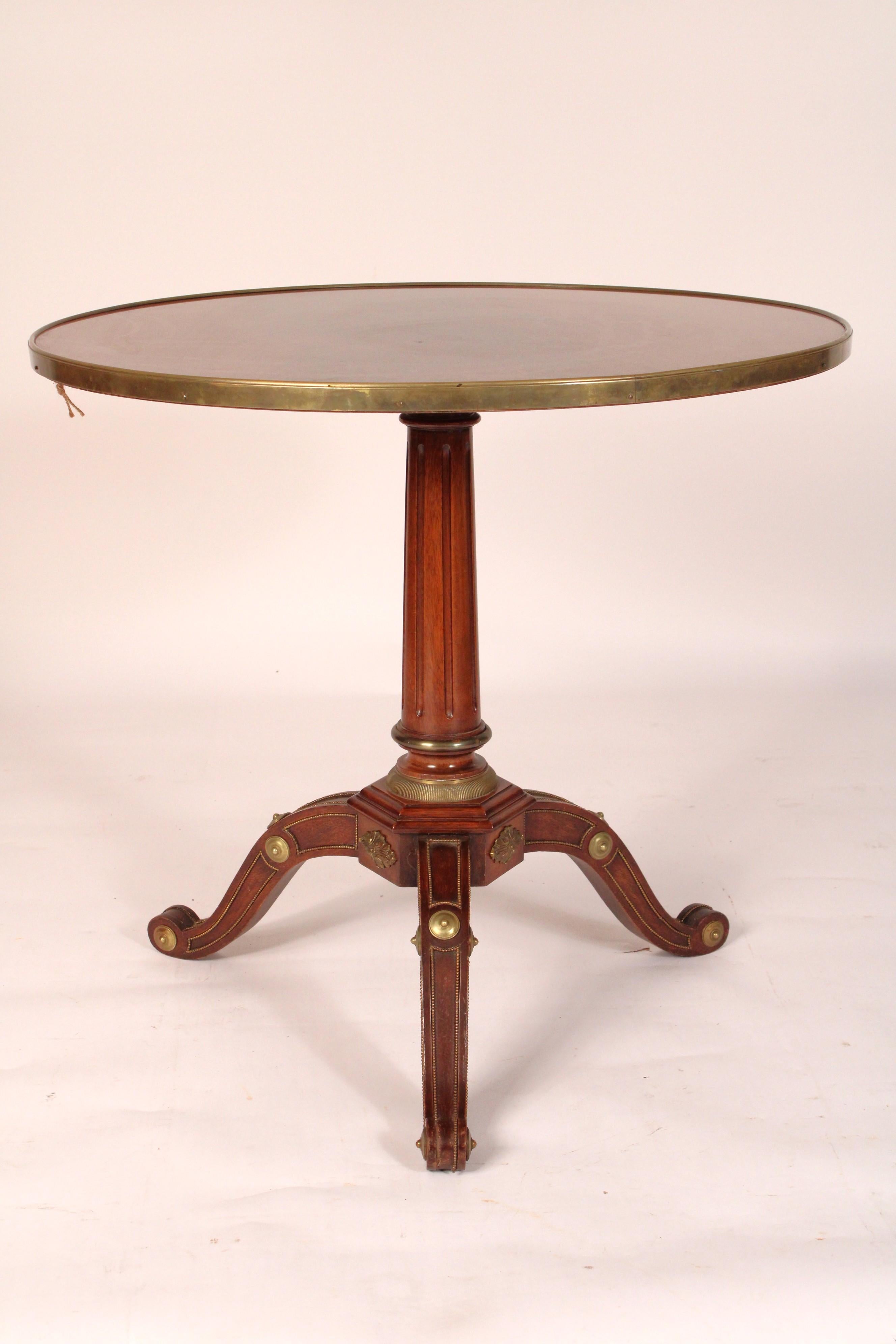 Gueridon antico in stile Directoire con montatura in ottone e mogano, anni '20 circa. Con un piano in mogano a fiamma con bordatura in ottone sul bordo esterno, un piedistallo scanalato e tre gambe a slancio verso il basso con montature in ottone.