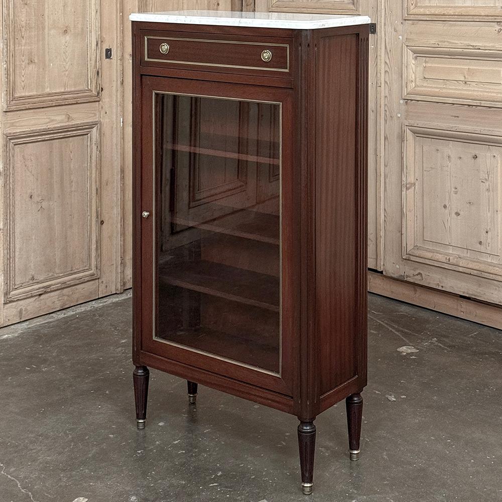 Antique Directoire Style Mahogany Petite Vitrine with Carrara Marble was hand-crafted in the mid-1900s out of exotic imported mahogany, then trimmed in brass and fitted with brass drawer and cabinet knobs, then finally topped with elegant Carrara