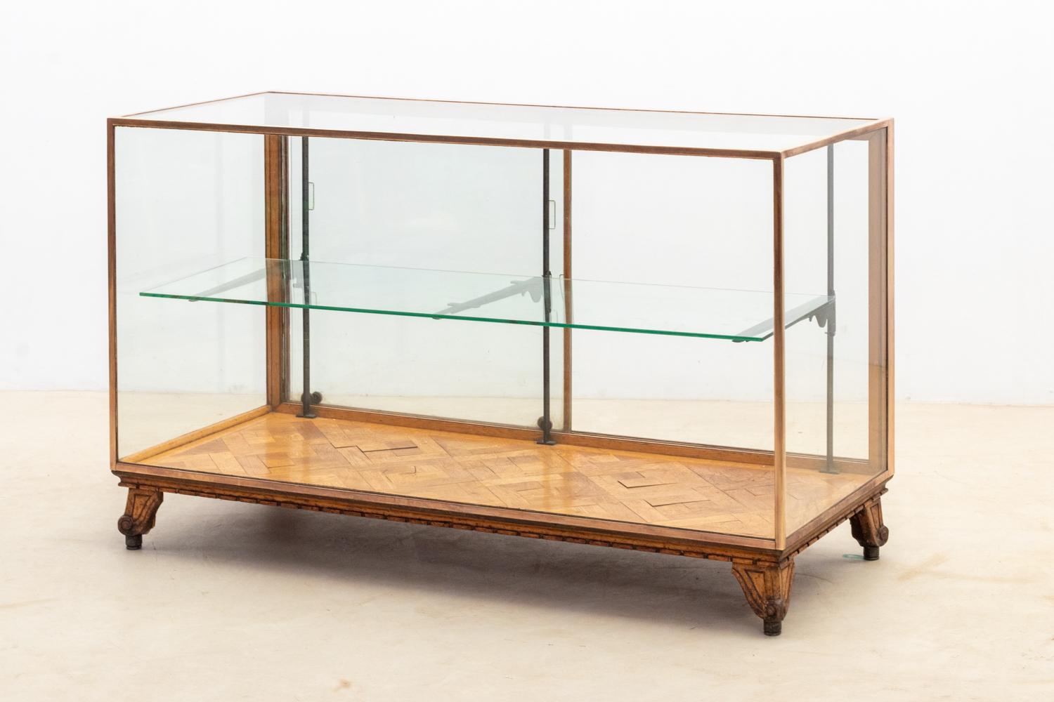 This classic antique display cabinet/shop counter, is a piece crafted from oak and brass. 
It features two sliding doors on the backside, providing  functionality. 
The shelves within this cabinet are adjustable, allowing for customizable display