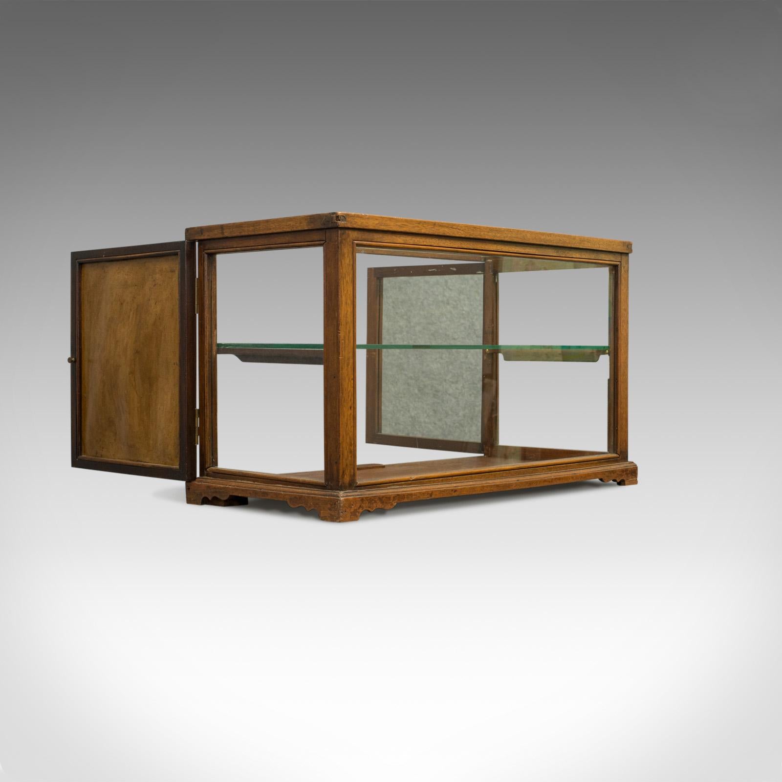 This is an antique display cabinet or shop fitting with a central glass shelf and mirror back. An English, Victorian oak cabinet from the late 19th century, circa 1900.

Crafted from oak and showing fine grain interest
Displays a desirable aged