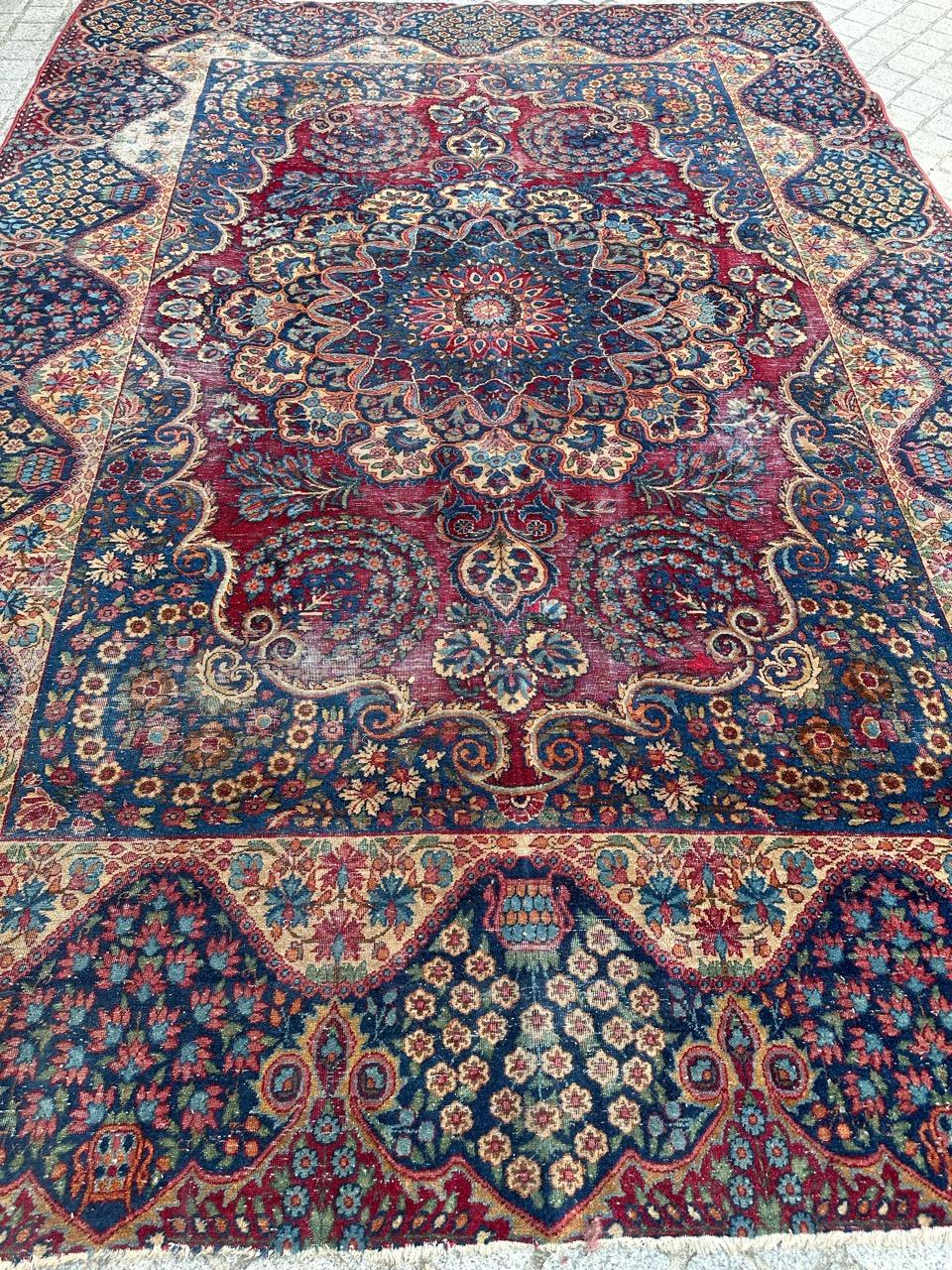 Exquisite late 19th-century antique distressed Kirman rug. This masterpiece features a stunning floral design in natural colors, meticulously hand-knotted with wool velvet on a cotton foundation. The vibrant red background sets the stage for a grand