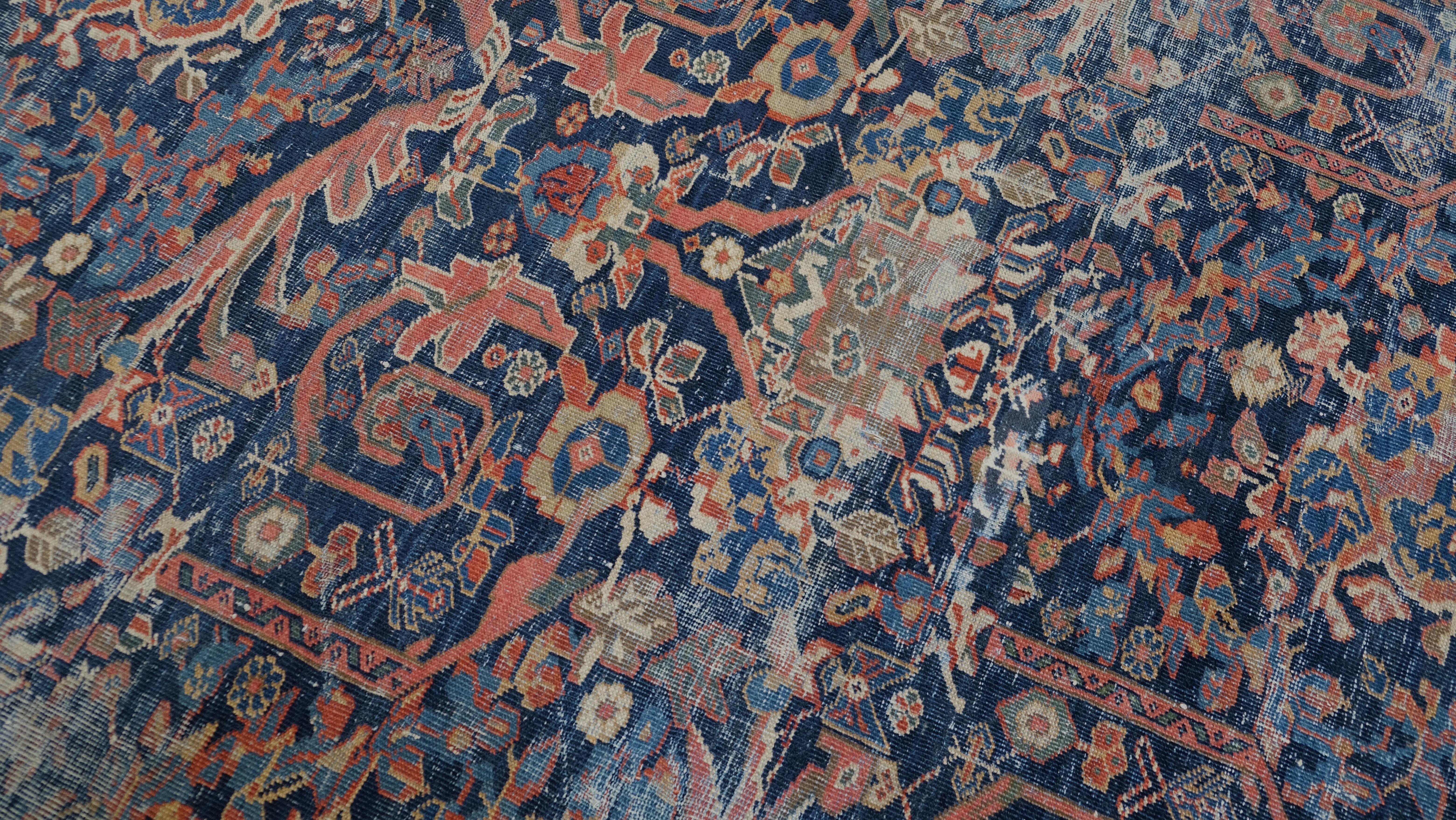 Dieser antike handgeknüpfte Wollteppich ist ein fesselndes Meisterwerk, das künstlerische Eleganz mit kultureller Bedeutung verbindet. Vor einem satten marineblauen Hintergrund schaffen die verschlungenen Muster und die leuchtenden Rot- und