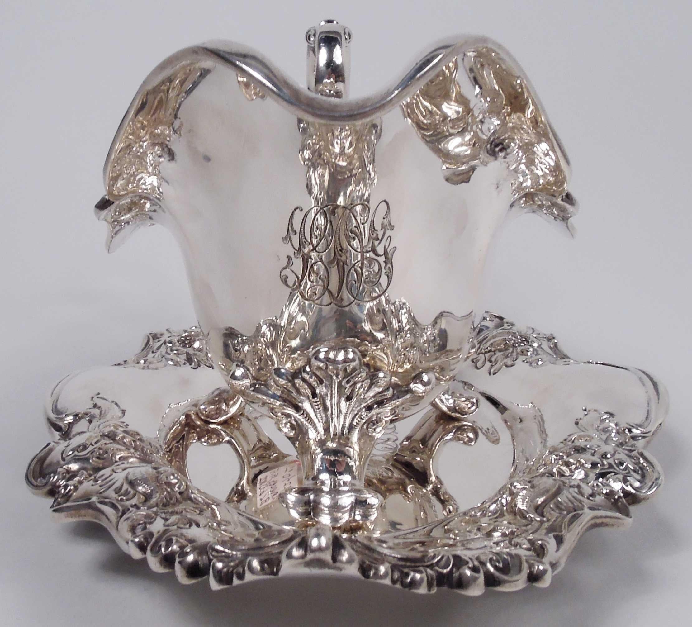 Edwardian Classical sterling silver gravy boat on stand. Made by Dominick & Haff in New York in 1907. Boat has helmet mouth, leaf-capped high-looping handle, and 3 leaf-mounted scroll supports. Stand has oval well. Turned-down and irregular scrolled