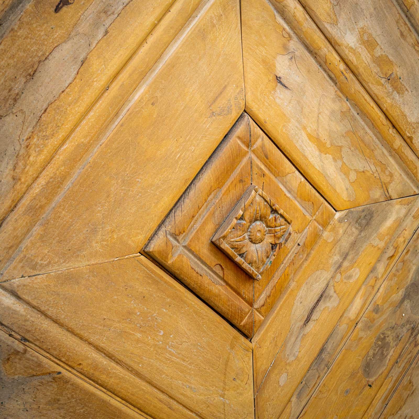 Antique wooden door with central carved rosette and chevron design. The top edge is slightly rounded. 