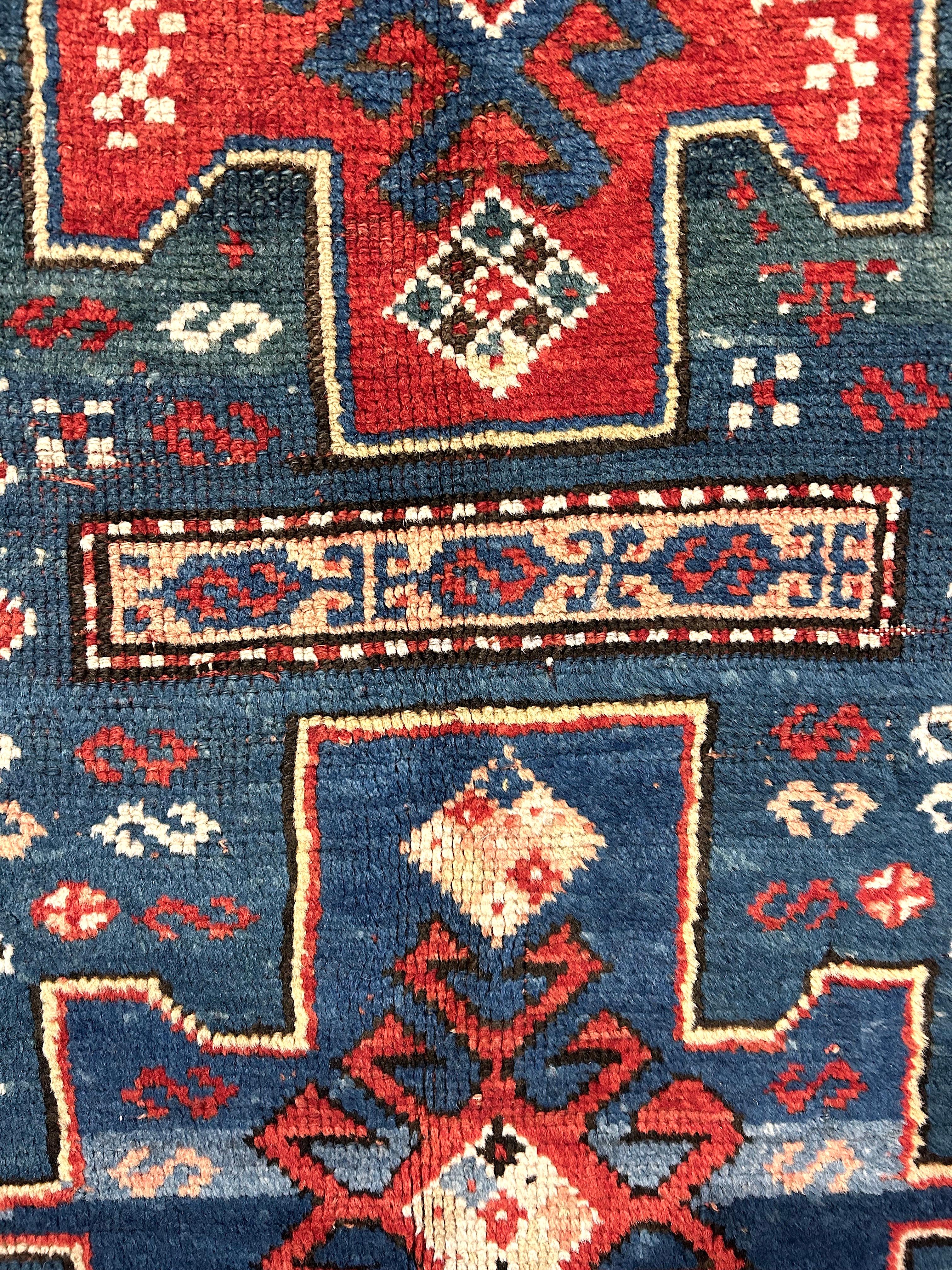 This dramatic and beautiful antique Kazak rug from the south Caucasus region has a composed, yet folky quality, with a hard to find blue/green field scattered with typical motifs, several animals and three large medallions.  The painterly quality of