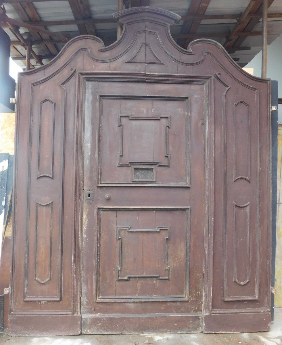 Ancient entrance door, double-sided main door in walnut, carved entirely by hand with very rich wavy shapes and sculpted panels, with original central door and grate (which belonged to a cloistered convent), ancient and original from the early 18th