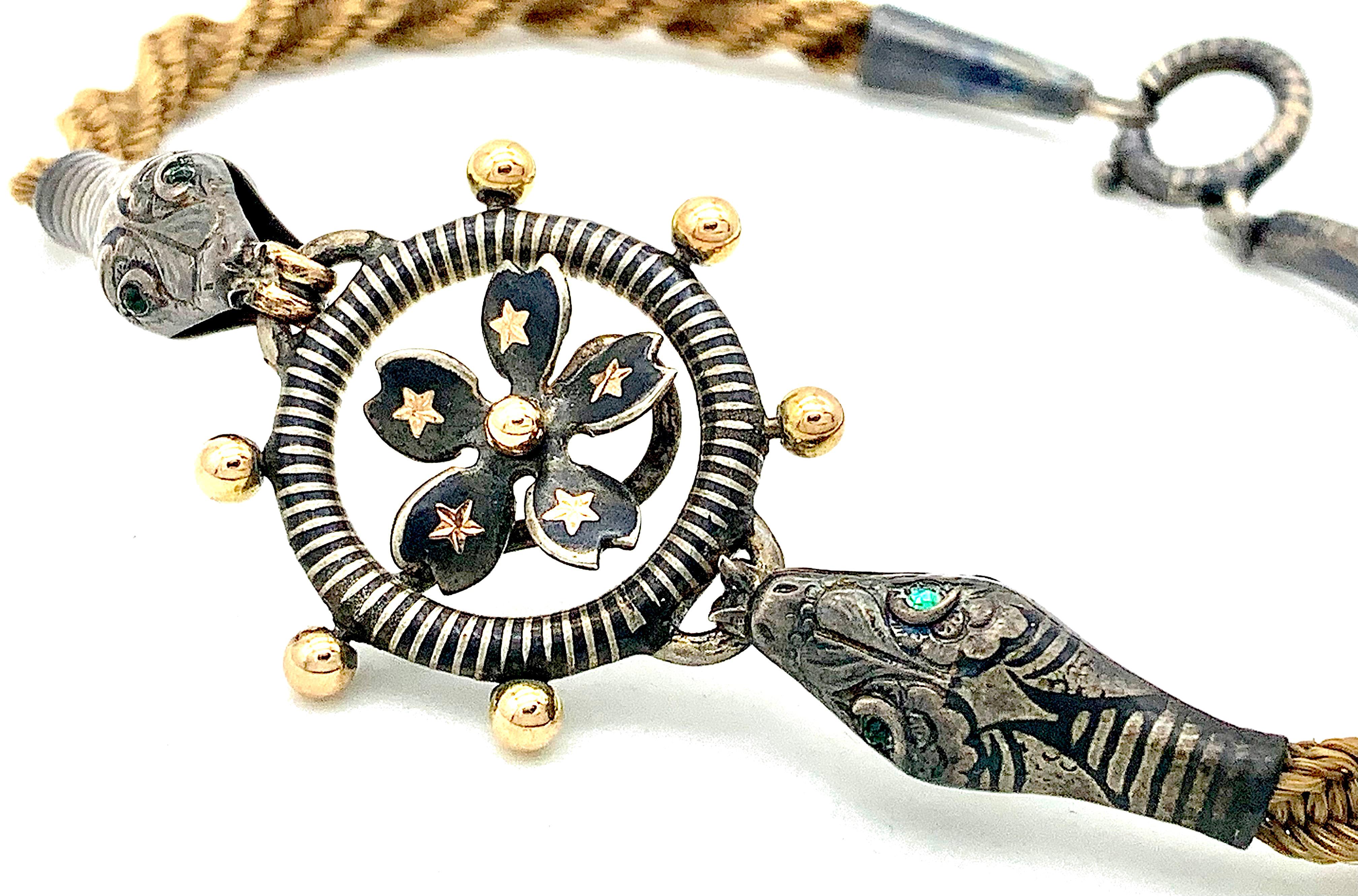 Ce bracelet rare et inhabituel est conçu comme deux têtes de serpent qui tiennent une roue.  Les boutons de la roue ont été recouverts d'une dorure à l'or rose. Le centre de la roue est décoré d'une fleur composée de cinq pétales en forme de cœur,
