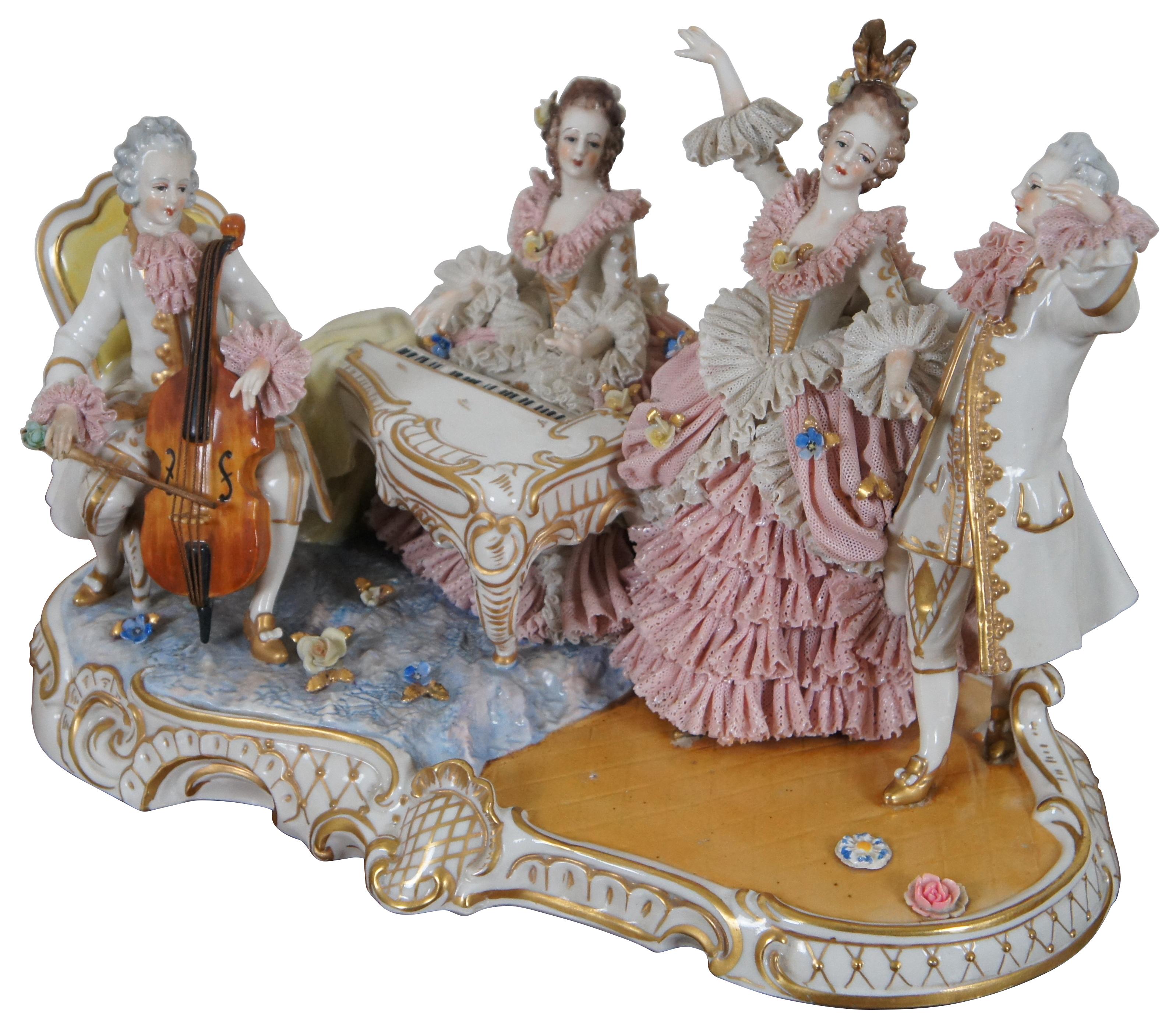 Antique late 1800’s Dresden capodimonte figure group showing two figures playing cello and harpsichord/piano forte while two other figures dance, swathed in flounces of pink and white porcelain lace, gilded accents and applied flowers.
 