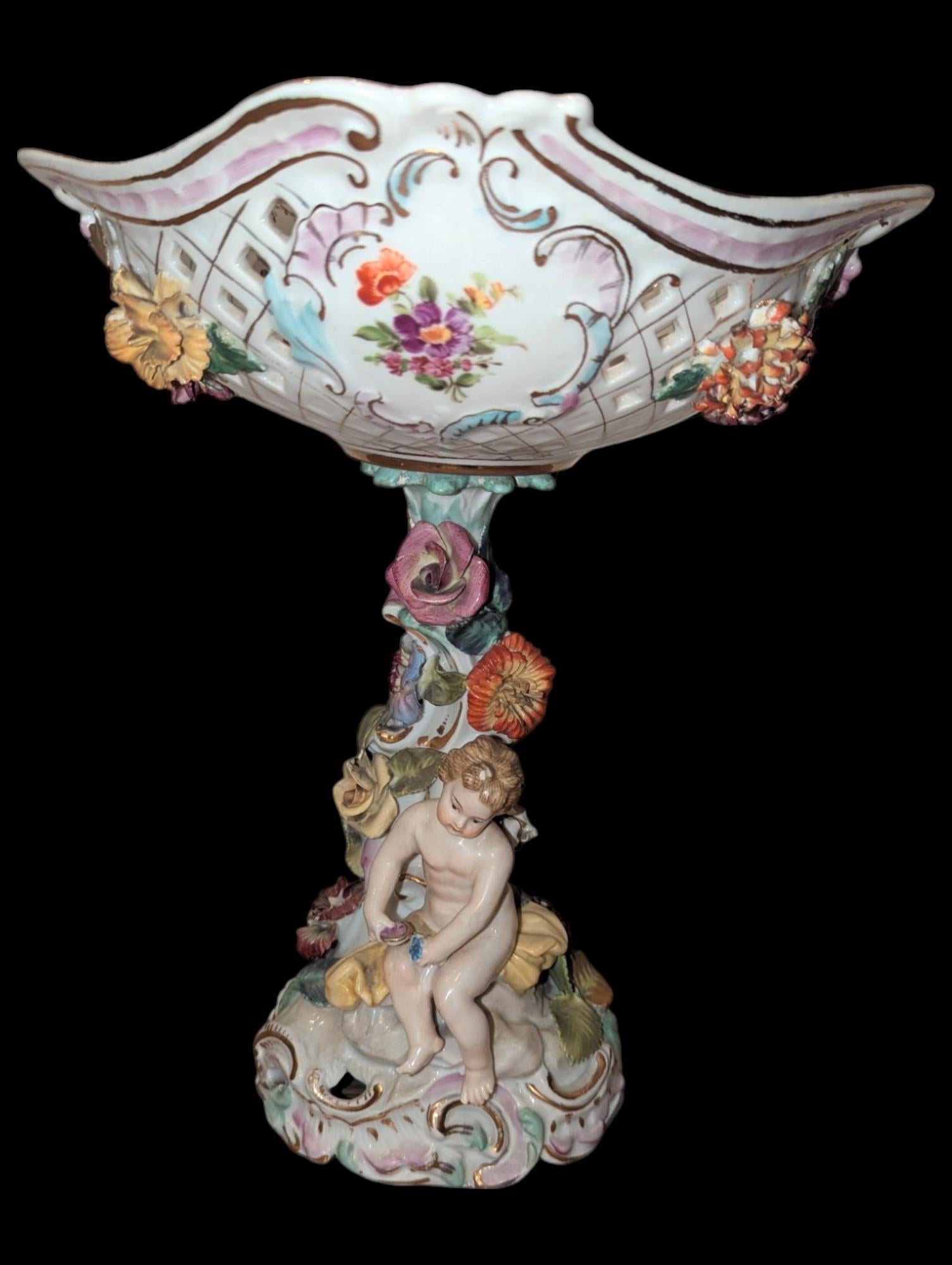 This Antique Dresden Figural Floral Encrusted Porcelain Compote is a masterful example of 19th-century European porcelain artistry. Created in the renowned Dresden style, this piece features a captivating blend of delicate hand-painted details,