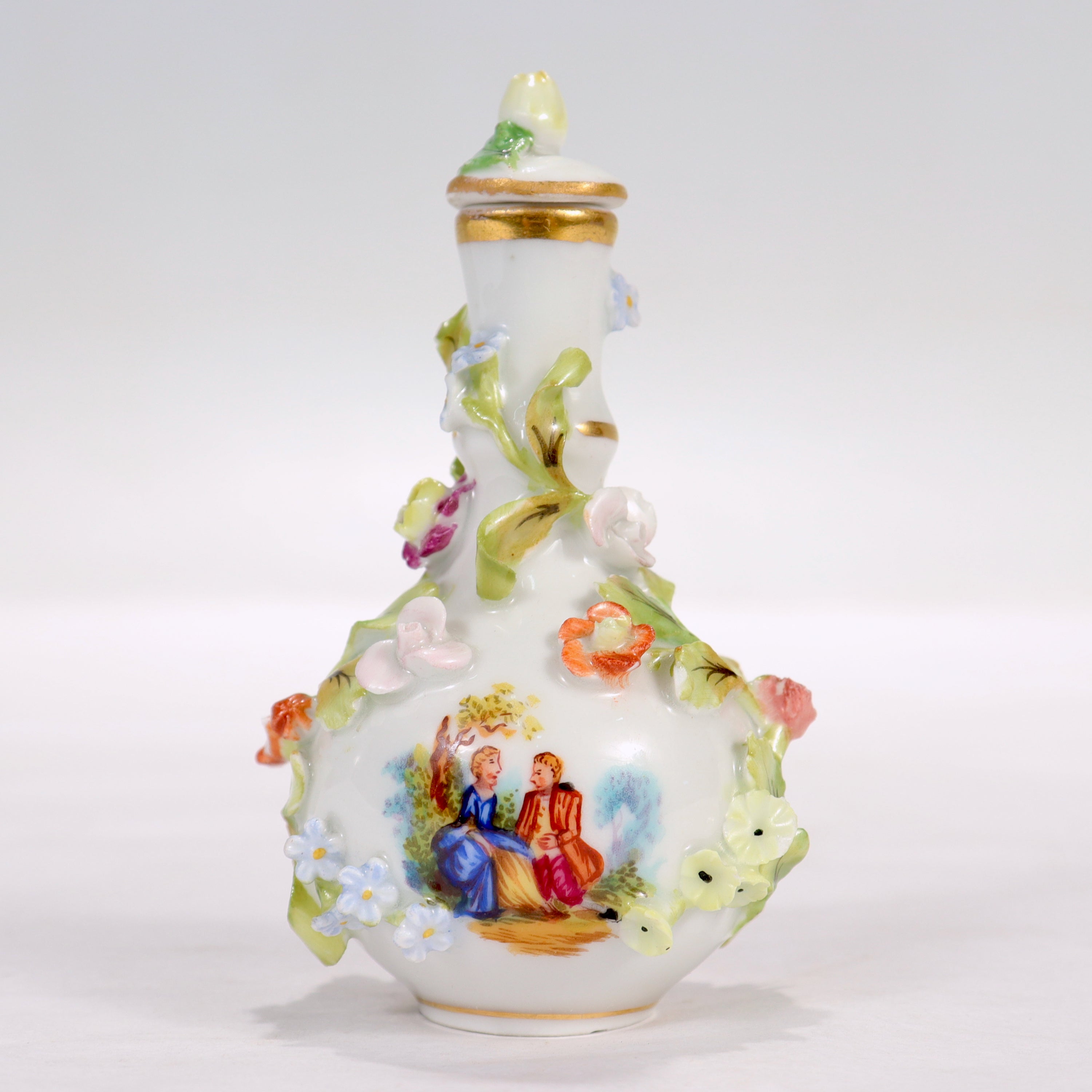 A fine antique miniature Dresden porcelain perfume bottle.

By Thieme Potschappel.

Decorated throughout with encrusted porcelain flowers and painted scenes. One side of the bottle is painted with flowers, the other with a scene of a gallant and
