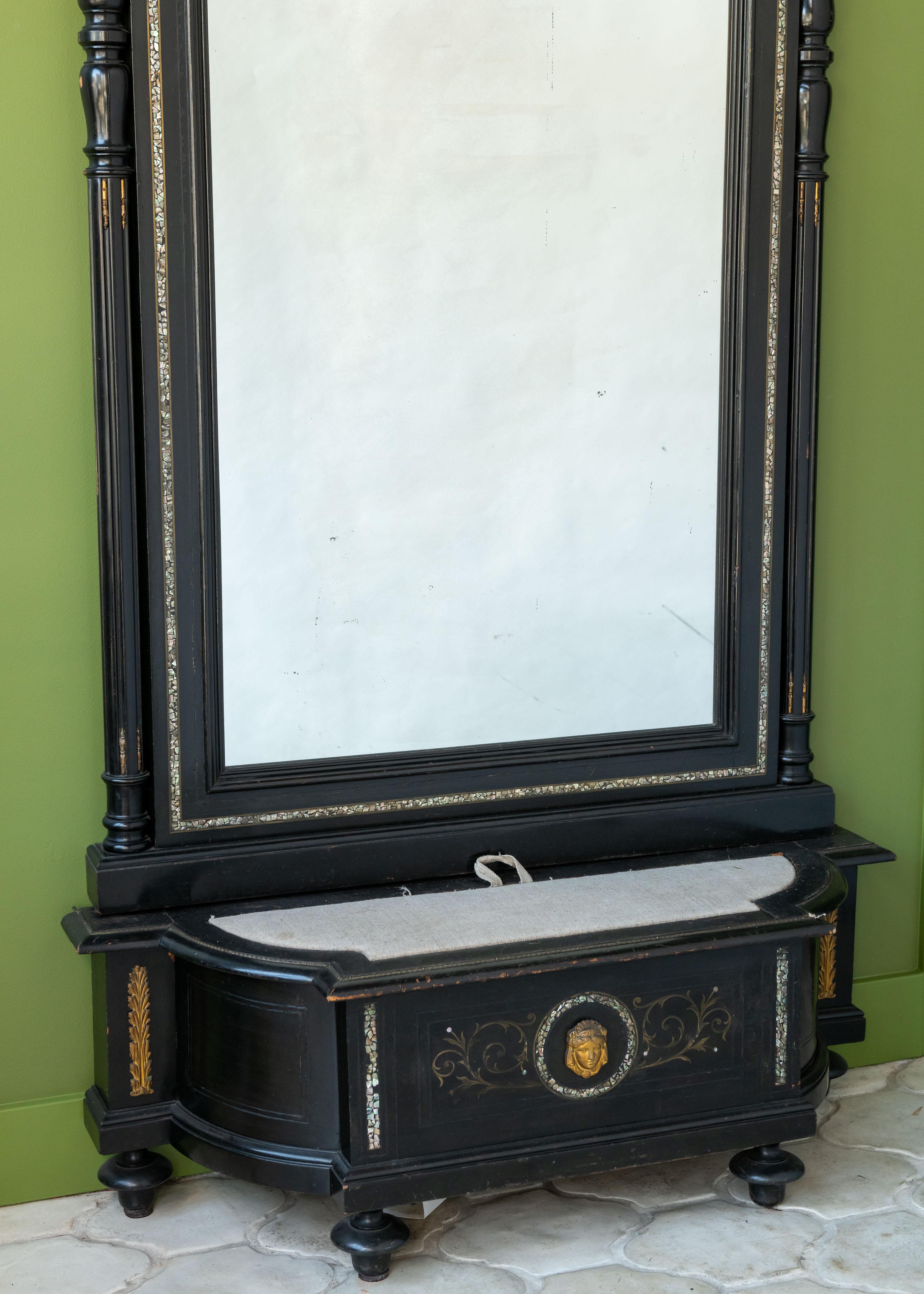 Este espejo francés de estilo Napoleón III se caracteriza por sus líneas rectas y su madera lacada en negro, con elaboradas composiciones decorativas doradas en pan de oro en el frontón. La parte inferior del espejo incluye una consola baja,