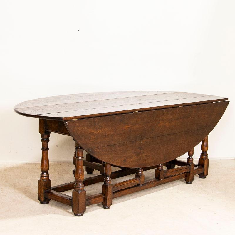 This handsome gateleg dining table is also known as an English wake table with drop leaves. Notice the dark patina of the oak, aged and naturally distressed over generations of use and lovely turned legs. The large oval shaped top has 2 drop leaves,