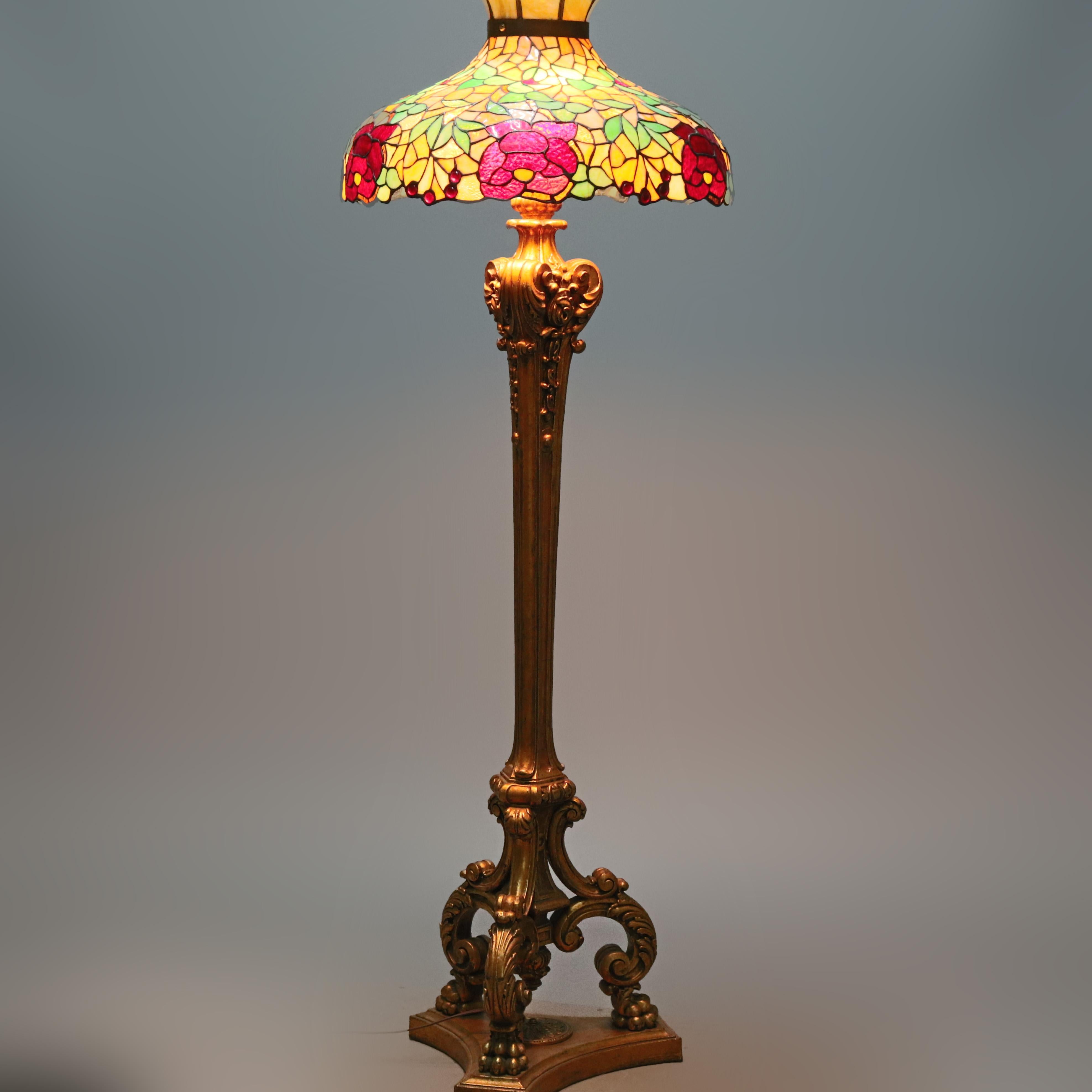 An antique mosaic floor lamp in the manner of Duffner & Kimberley, New York offers domed leaded stained with fiery glass, slag and jeweled glass shade with foliate, floral and cherry motif surmounting bronzed cast triple socket base having flared